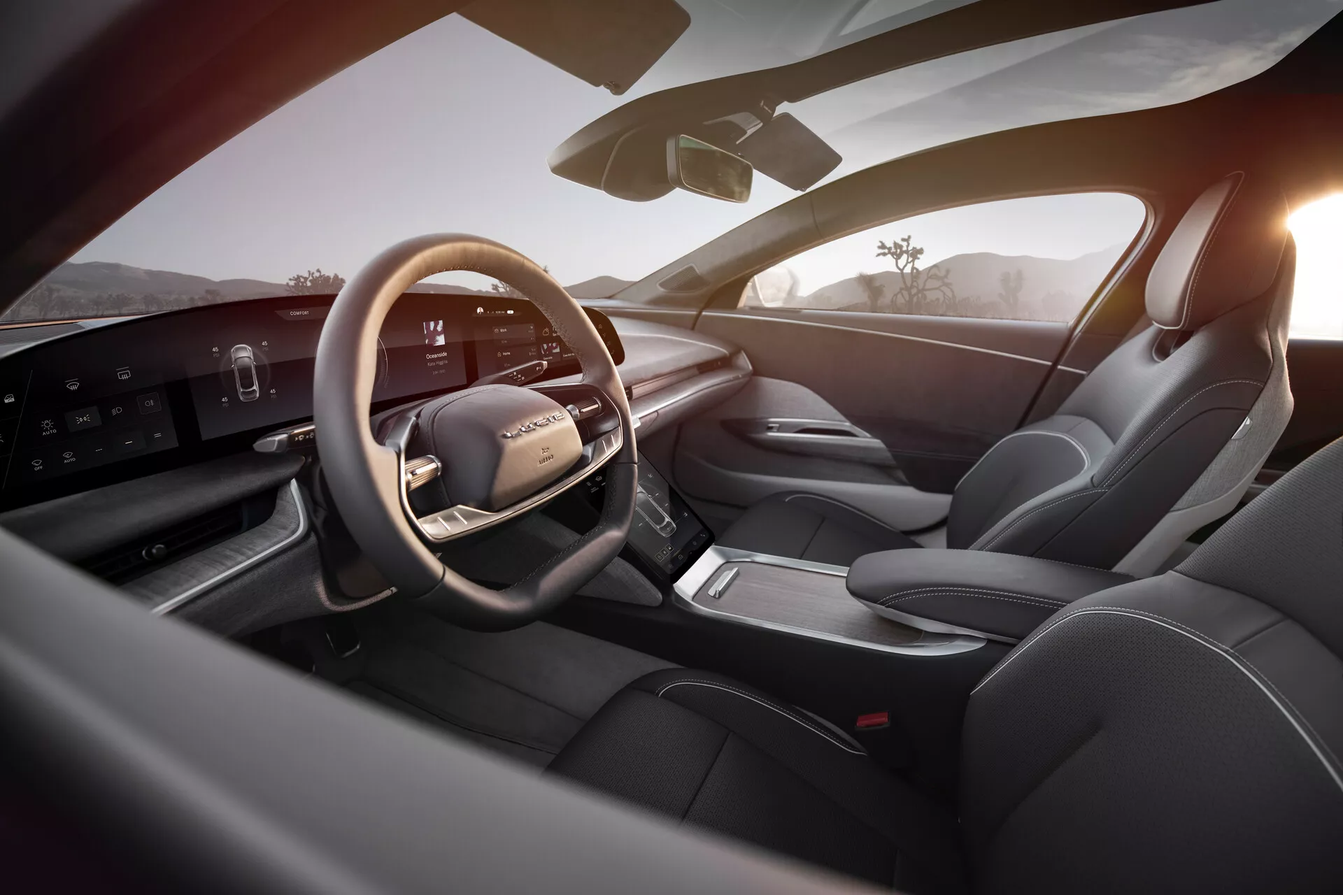 Pohled na interiér vozu Lucid Air 2022 z pohledu sedadla vzadu vpravo, ukazuje luxusní a moderní oblast řidiče. Hlavní prvky zahrnují kožený multifunkční volant s ovládacími prvky, štíhlý horizontální digitální přístrojový panel, minimalistickou středovou konzoli s elektronickým voličem převodovky, sportovní sedadla čalouněná kůží, sofistikované ovládací prvky na dveřním panelu a celkově dobrou viditelnost s bočním zrcátkem a čelním sklem. Dobře osvětlený interiér zdůrazňuje špičkovou technologii a prémiový design, zvýrazněný teplým venkovním světlem naznačujícím východ nebo západ slunce.