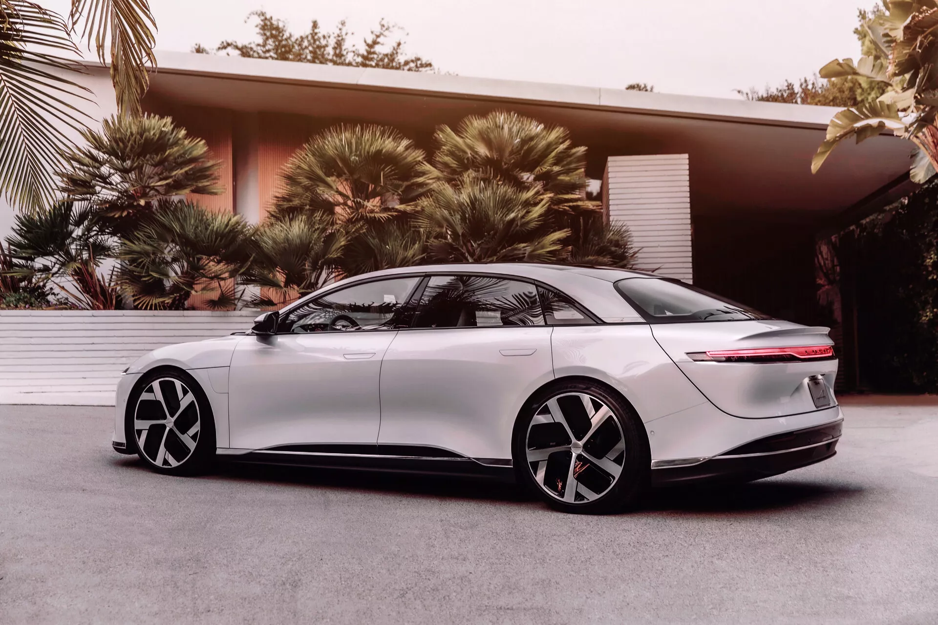 2022 Lucid Air elektrický sedan, 1. generace, boční profil z nízkého úhlu zdůrazňující aerodynamický design, elegantní LED světlomety, hladký přední blatník, zatahovací zapuštěné kliky dveří, dvoutónová pětispokea kola z lehké slitiny, tónovaná okna, zadní část ve stylu fastback s vodorovným světelným pruhem a integrovaným spoilerem, představující moderní technologii a design elektrických vozidel.