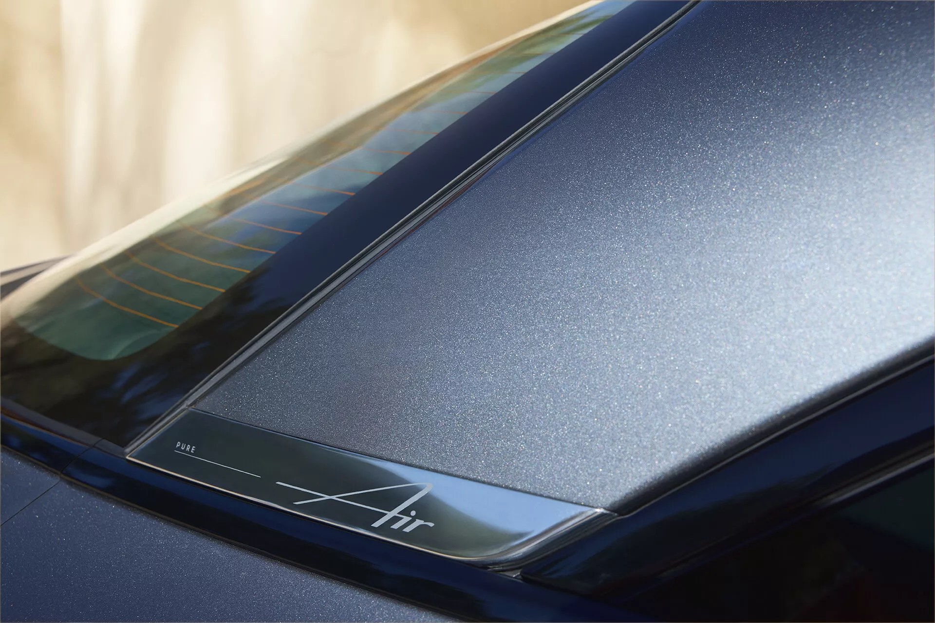 Detailní záběr zadní části u střechy vozu Lucid Air 2022 (1. generace), zobrazující tmavě modrý lesklý povrch a elegantní aerodynamické linie. Obsahuje podsvícený proužek s nápisem 'Air', který zdůrazňuje luxusní design a možnou pokročilou technologii.