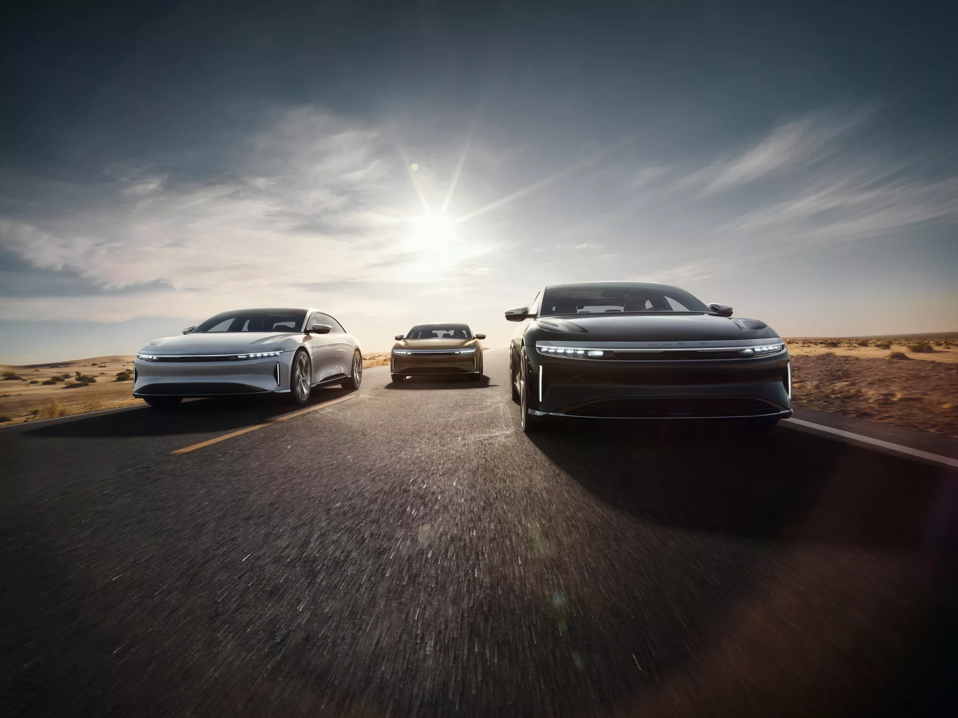 Přední pohled na Lucid Air 2022 s aerodynamickým designem a LED světlomety ve stupňovité formaci na asfaltové silnici s pouští v pozadí, sluneční světlo vrhá teplý zář