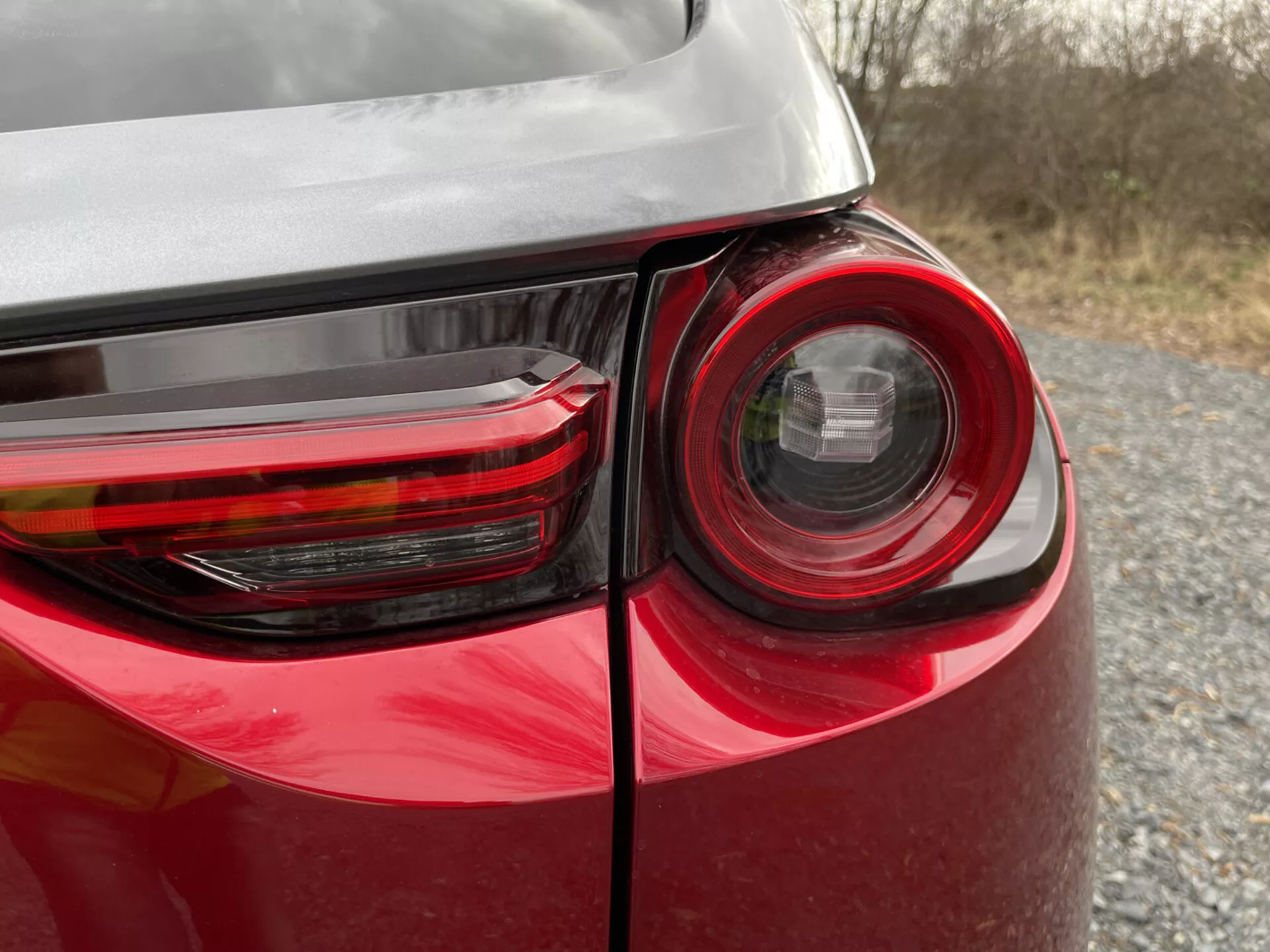 Detailní pohled na zadní roh vozidla Mazda MX-30 2020 s detailním designem zadních světel, lesklým červeným lakem a odrazem na jeho karoserii, což zdůrazňuje moderní technologii osvětlení a design vozidel.