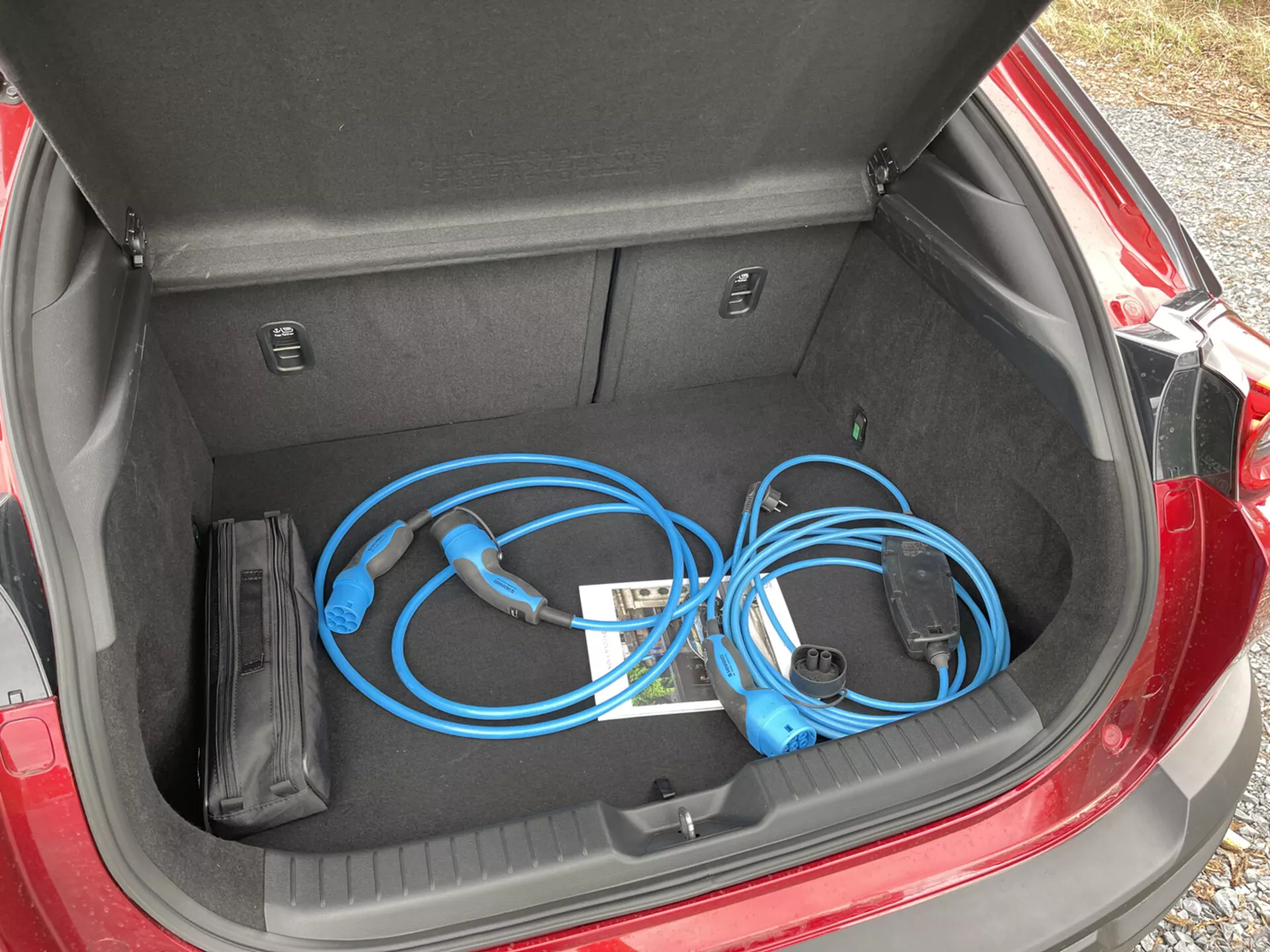 Otevřený kufr Mazda MX-30 2020 s přenosným nabíjecím kabelem pro elektrická vozidla, zblízka, z horního pohledu zleva, předvádějící čistý a rovný prostor pro ukládání spolu s vnitřními přihrádkami.