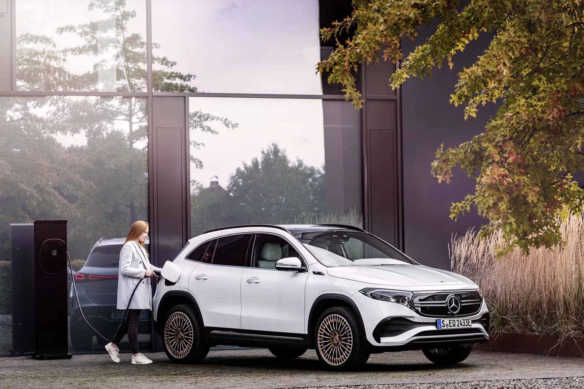 Mercedes-Benz EQA 2021 zaparkovaný u nabíjecí stanice pro elektromobily, prezentuje jeho elegantní bílý design, aerodynamický vzor kol a hybridní schopnosti v udržitelném prostředí