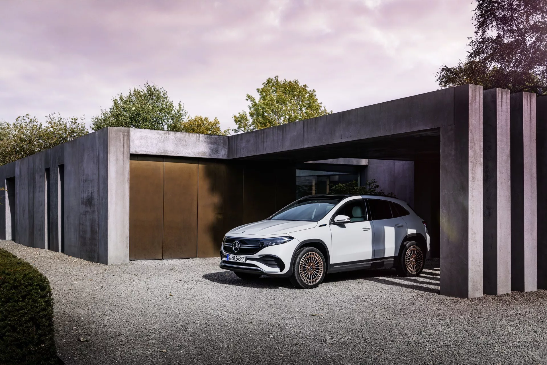 Mercedes-Benz EQA 2021 zaparkovaný u vchodu minimalistické budovy, který zobrazuje jeho pohled ze tří čtvrtin vpředu v jemném denním světle, zdůrazňující jeho elegantní aerodynamický design, LED světlomety, vysokou linii ramen, siluetu podobnou kupé, zapuštěné kliky dveří, složitě navržená slitinová kola a potenciál pro pokročilé asistenční systémy řízení.