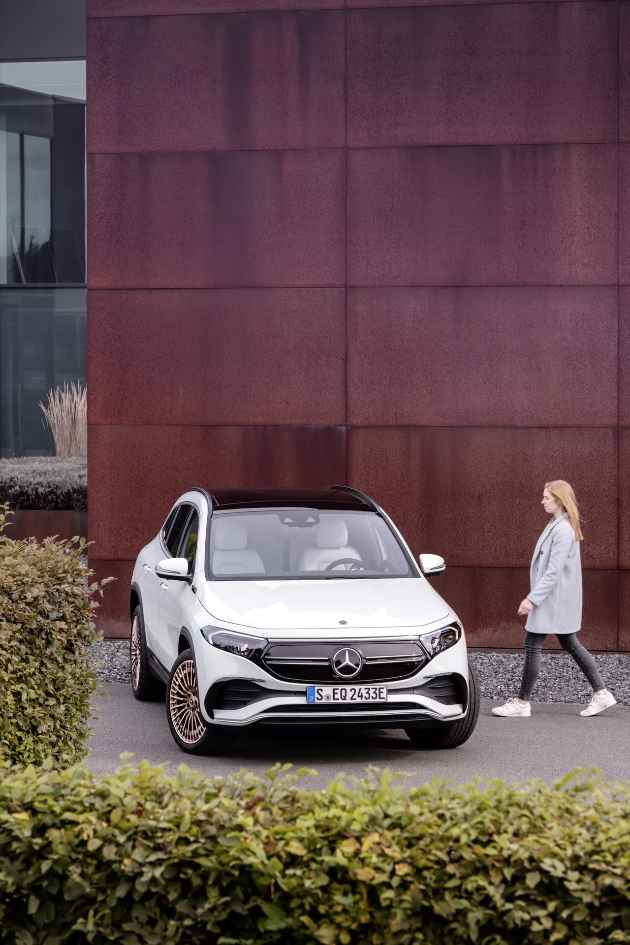 Mercedes-Benz EQA 250 z roku 2021 zaparkovaný v městském prostředí s výraznou fasádou budovy s červenými panely, představující design elektrického kompaktního SUV a pokročilé funkce jako LED světlomety a aerodynamická kola