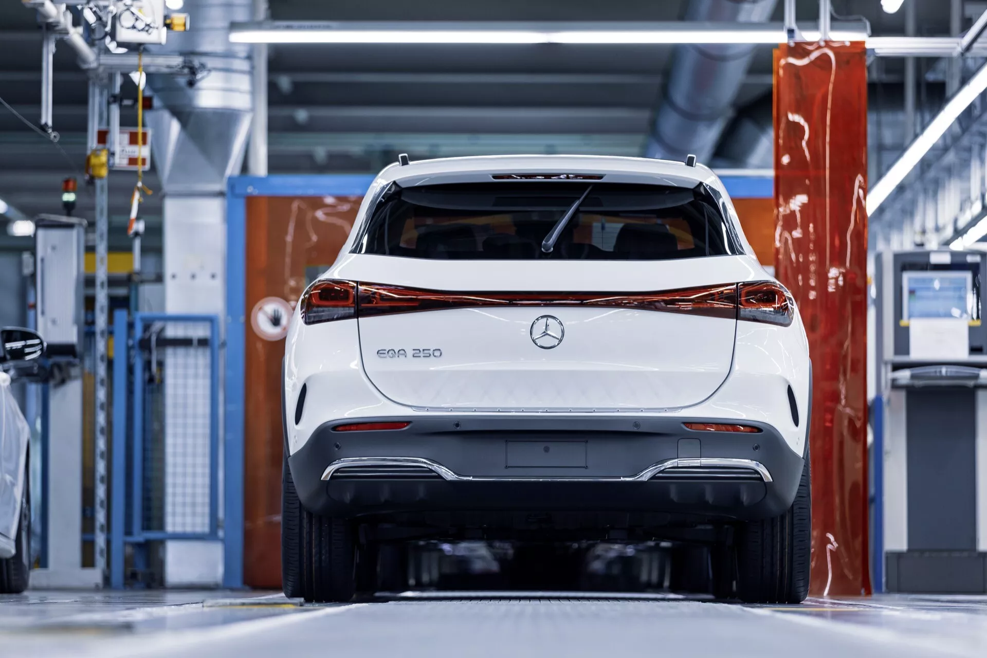 Zadní pohled na bílý elektrický vůz Mercedes-Benz EQA 250 v moderním průmyslovém prostředí, s důrazem na zadní světla, nárazník a značení Mercedes s jasným zaměřením na design a technologické vlastnosti.