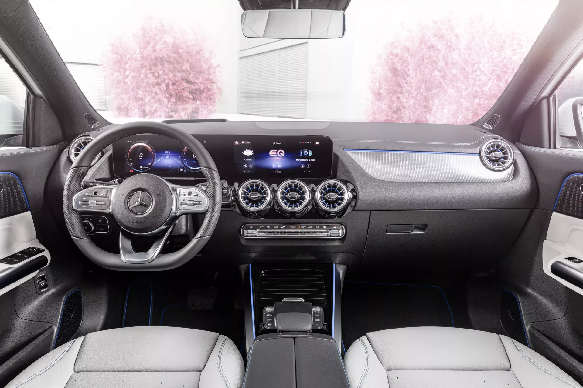Interiér Mercedes-Benz EQA 2021 s pohledem na palubní desku, multifunkční volant se stříbrnými prvky, digitální přístrojovou desku, širokoúhlý infotainment systém, kovově dokončené výdechy vzduchu, duální klimatizaci, moderní ovladač převodovky a luxusní sedadla z kůže ve dvoubarevném provedení se zdobným prošíváním z perspektivy zadního sedadla