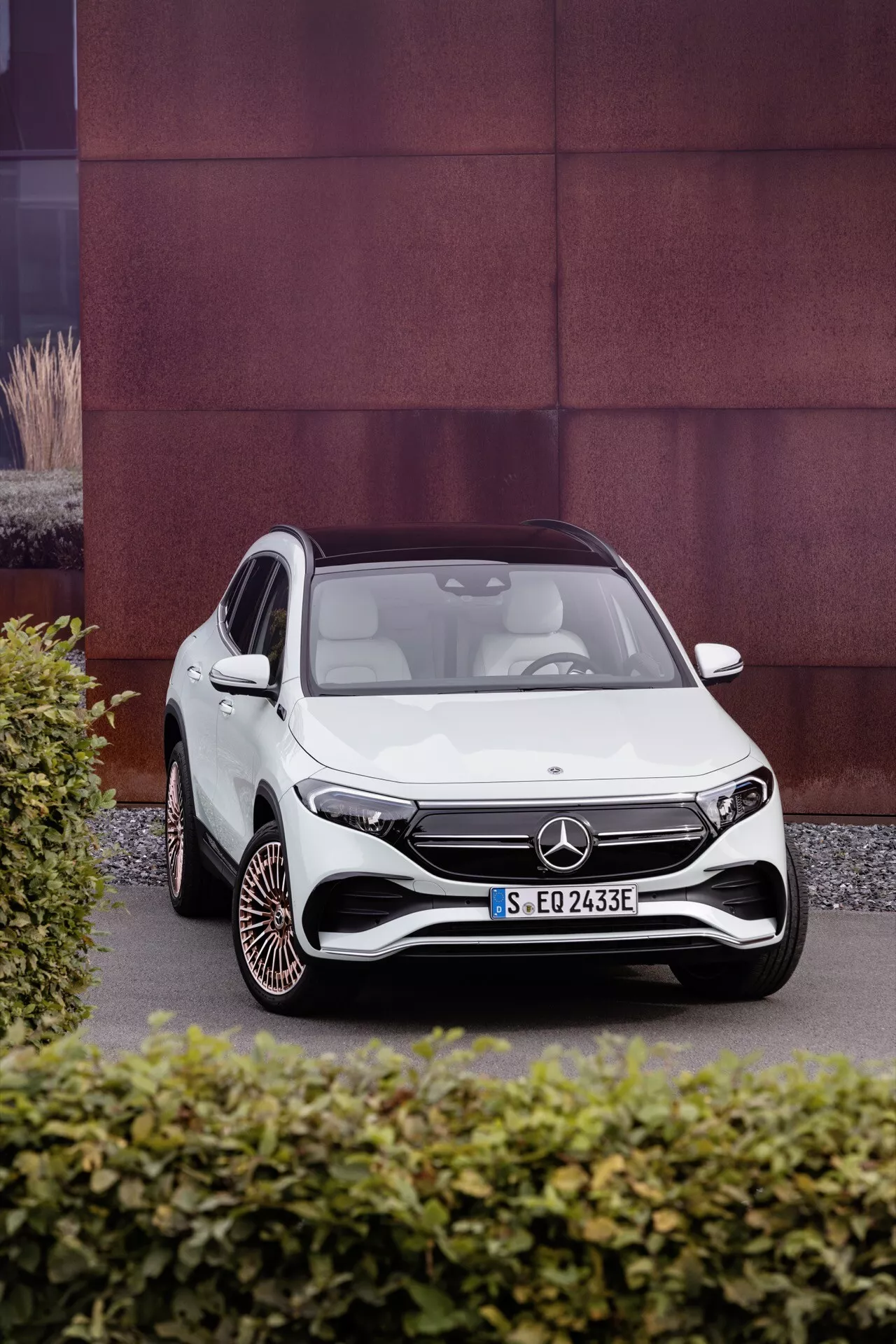 Bílý Mercedes-Benz EQA 2021, fotografovaný z čelního tříčtvrtečního úhlu, zobrazující aerodynamický design vozidla, LED světlomety, výraznou přední mřížku s velkým emblémem, sportovní přední nárazník a unikátní design kol na kontrastním texturovaném pozadí