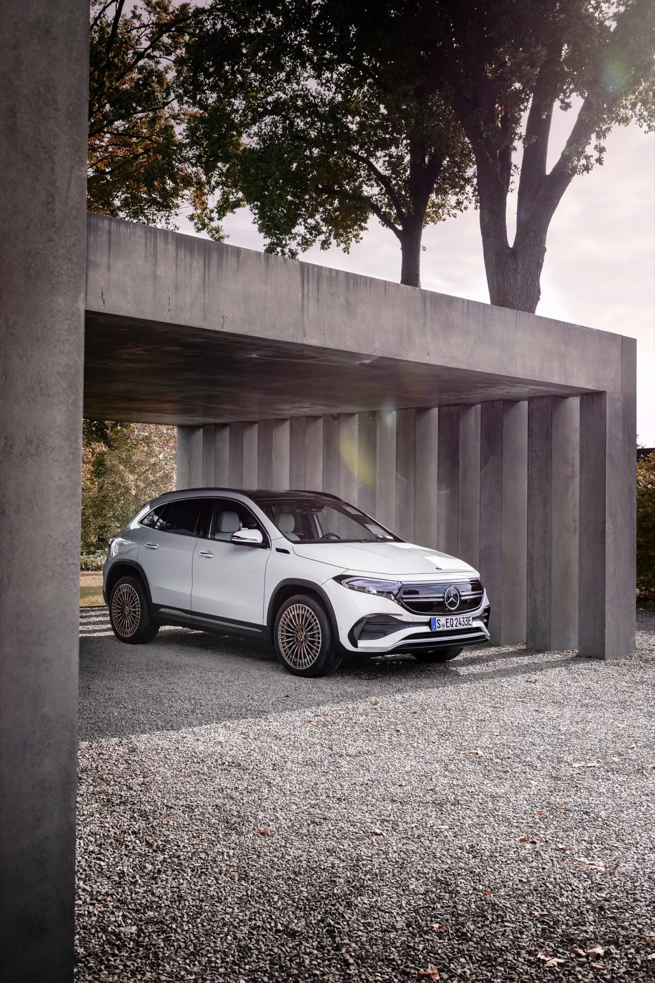 Mercedes-Benz EQA 2021 zaparkované pod minimalistickou betonovou konstrukcí, zobrazující jeho elegantní LED světlomety, výraznou přední mřížku se znakem, aerodynamické bílé karoserie a složité slitinové kola z nízkého úhlu tříčtvrtečního předního pohledu.