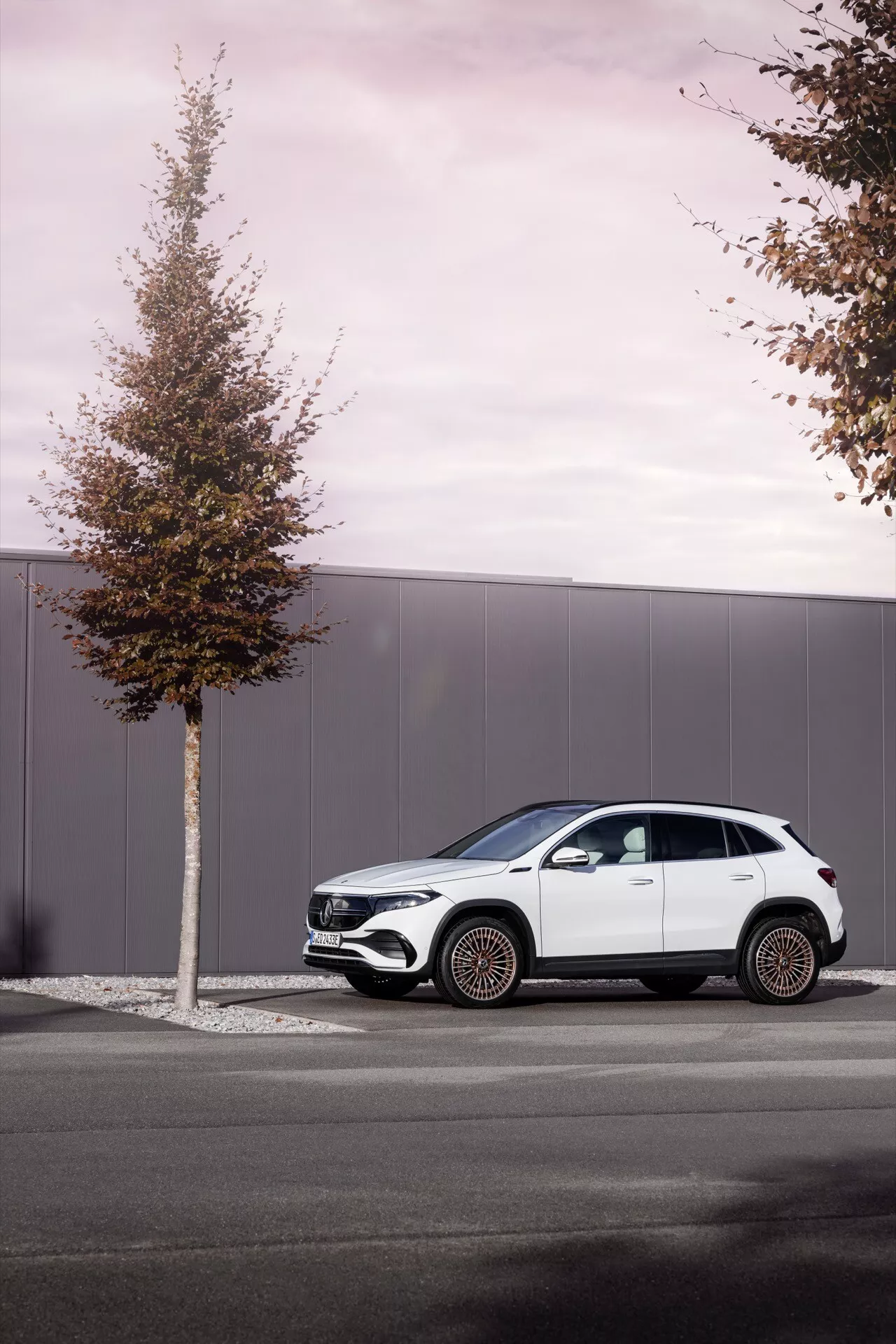 Boční profil Mercedes-Benz EQA 2021 zaparkovaný na městské ulici, předvádí moderní design SUV s tekoucími liniemi, výraznými koly, kontrastním černým lemem a vícepaprskovými slitinovými koly na pozadí zamračeného dne
