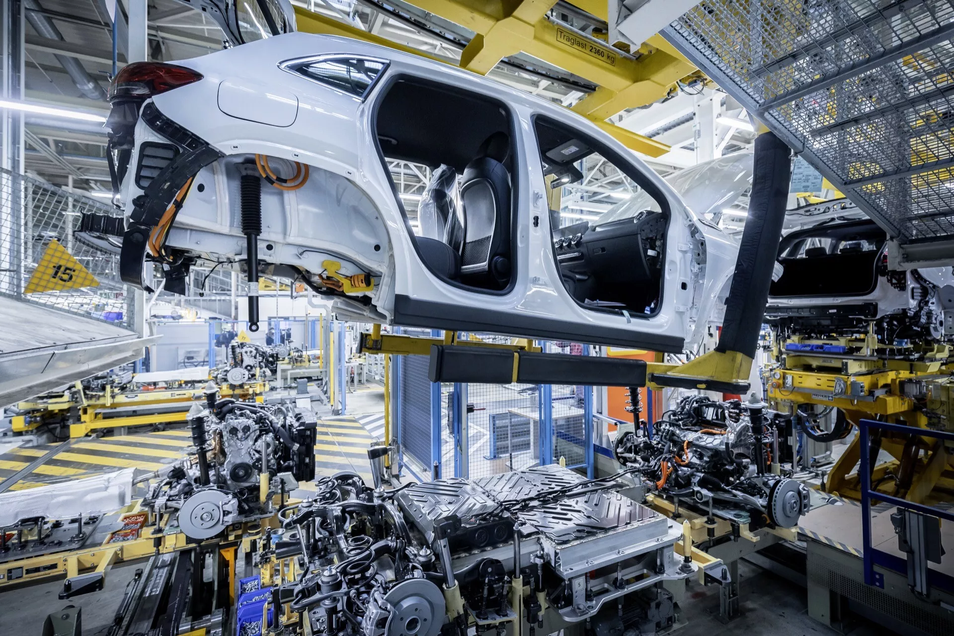 Bílý Mercedes-Benz EQA (243) z roku 2021, který je ve fázi montáže v automobilovém závodě, ukazuje na svou karoserii, podvozek a pokročilou technologii robotické montáže