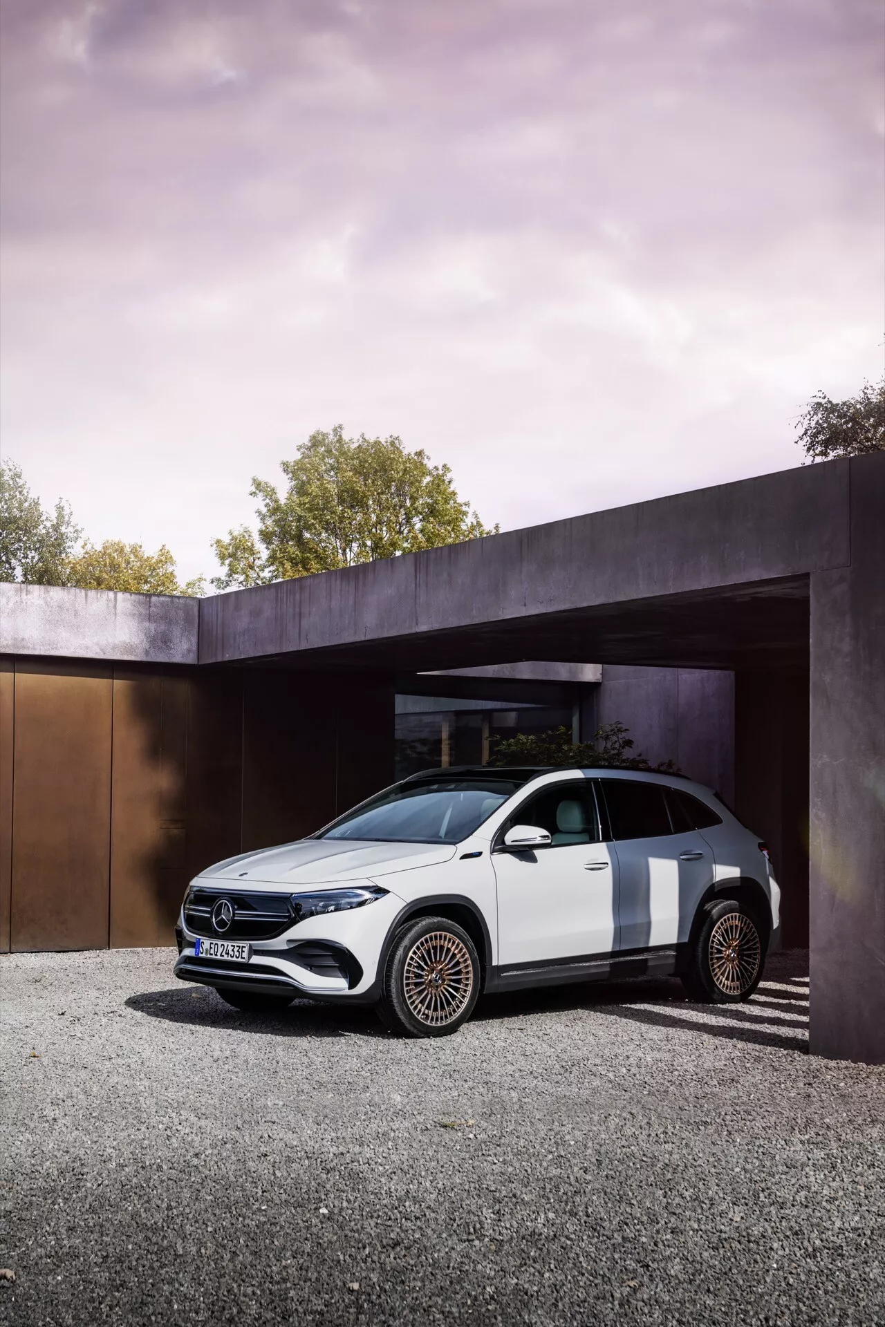 Mercedes-Benz EQA 2021 zaparkovaný pod moderní architektonickou strukturou brzy ráno nebo pozdě odpoledne prezentující luxusní designové prvky jako lesklý černý přední gril, LED světlomety a unikátní bronzová kola