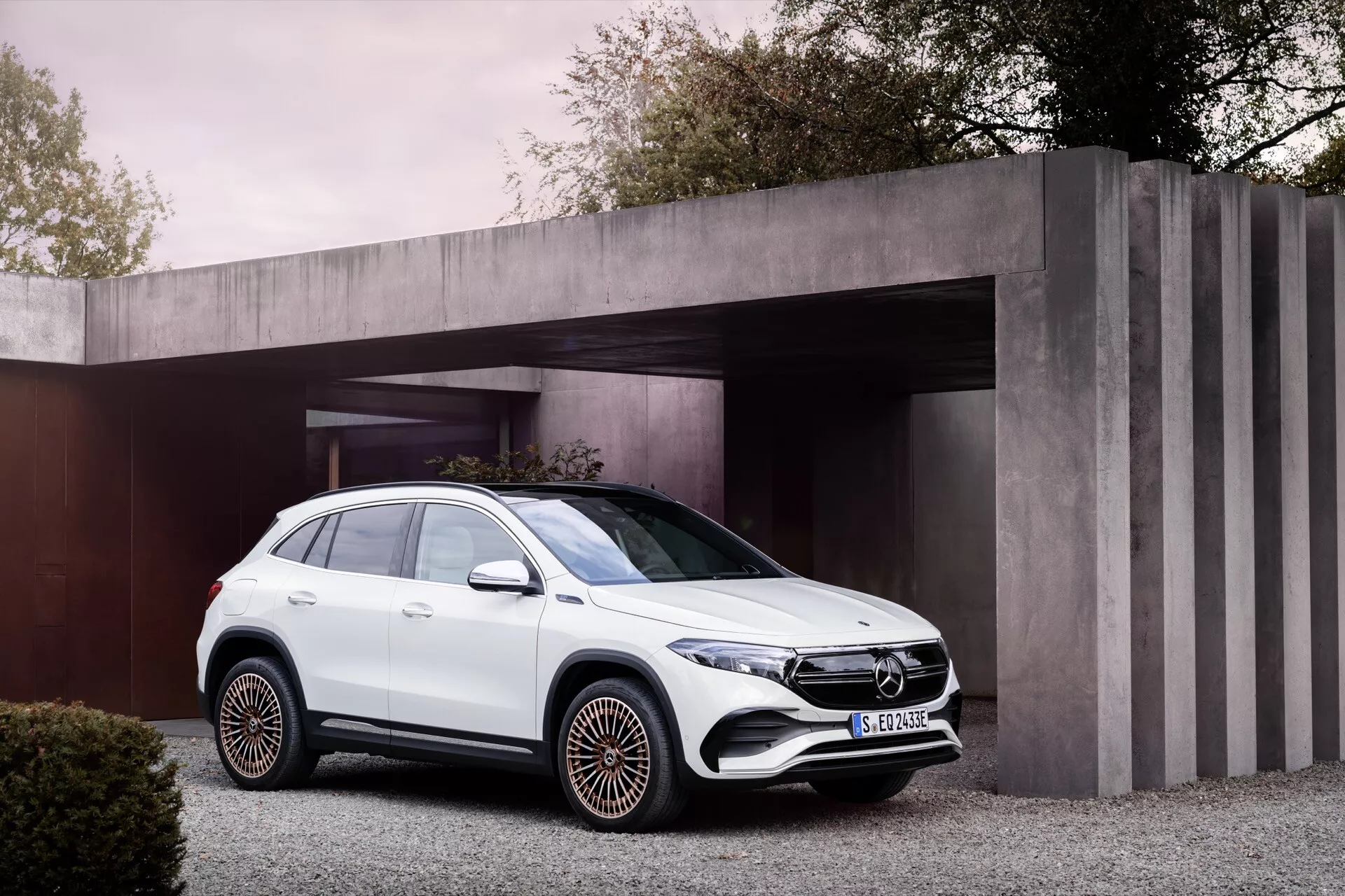 Bílé SUV Mercedes-Benz EQA 2021 zaparkované na moderním příjezdovém cestě s pozadím stylizovaného rezidenčního přístřešku, zdůrazňující pohled z přední trojčtvrtě na jeho přední mřížku, LED světlomety, boční karoserii, kola a okna