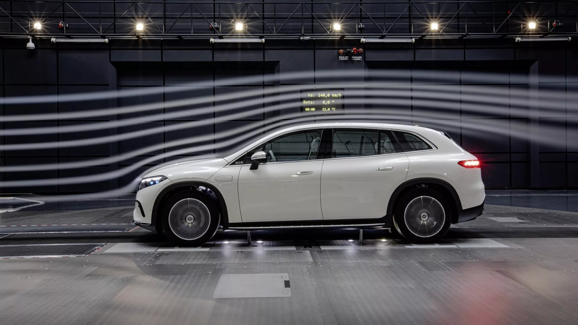 Boční profilový pohled na Mercedes EQS SUV 2022 na zážitkové trati, zdůrazňující jeho elegantní design, slitá kola a reflexní, dobře udržovanou karoserii. Moderní luxusní crossover SUV má střešní linii mírně klesající vzadu, což naznačuje sportovní estetiku kombinovanou s praktičností SUV. Fotografie zachycuje celou délku vozidla s rozmazanými čarami v pozadí simulujícími vysokou rychlost, zdůrazňující design a předpokládaný výkon vozidla v kontrolovaném, monochromatickém prostředí.