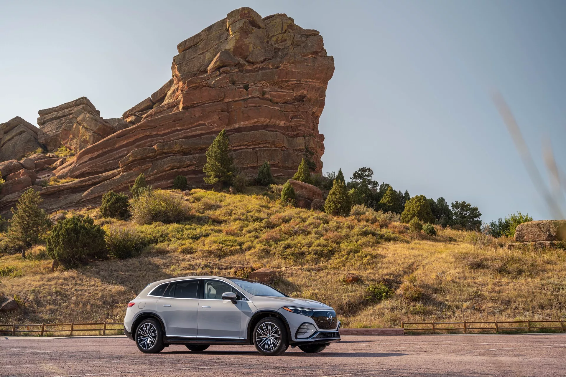 Boční profilový pohled na Mercedes EQS SUV 2022 zaparkovaný na dlážděné silnici s velkými skalními útvary v pozadí, zdůrazňující jeho vyšší světlou výšku, litá kola, elegantní designové linie, tónovaná okna a metalický lak.
