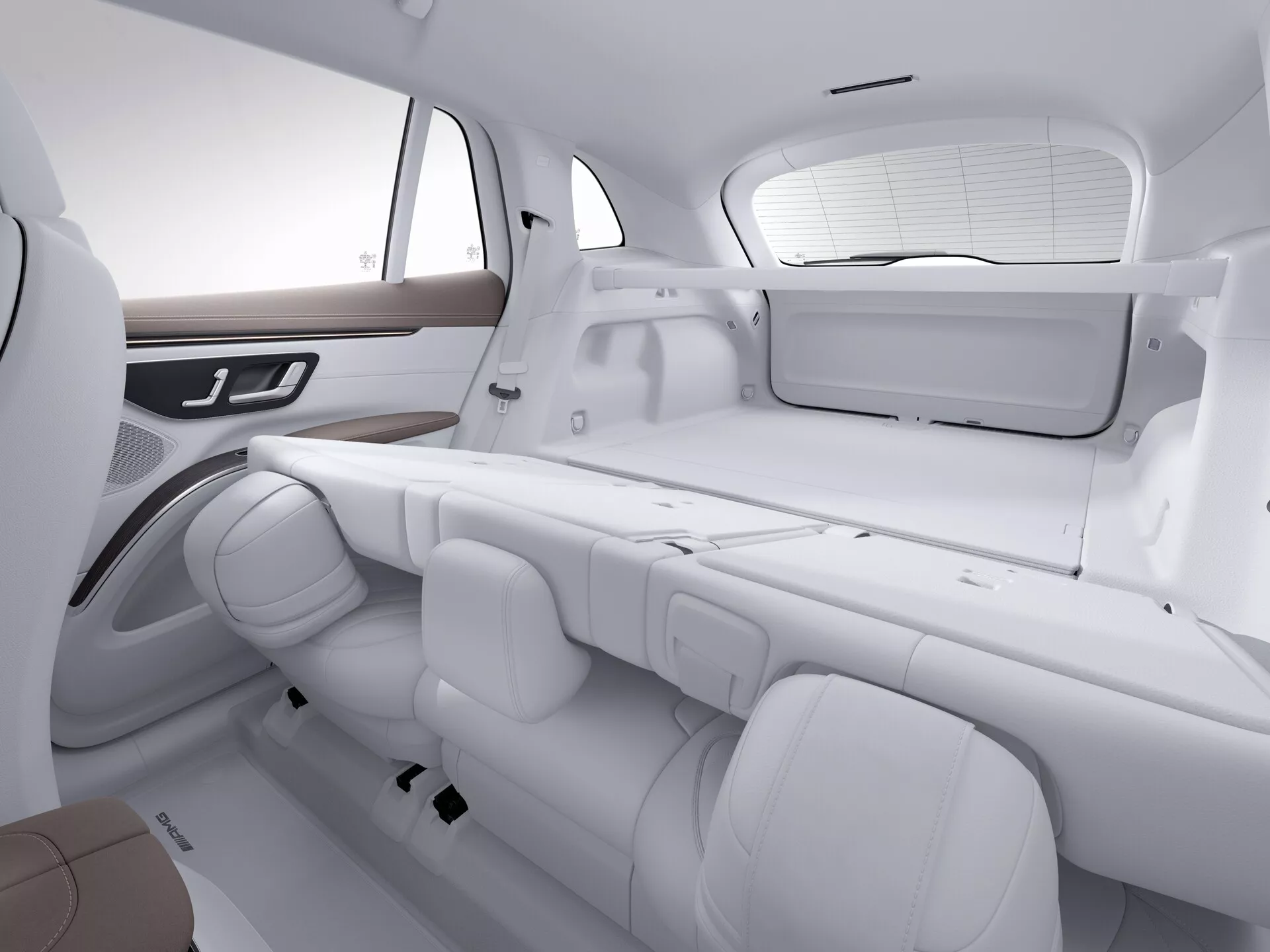 Pohled na interiér Mercedesu EQS SUV 2022 zaměřující se na zadní sedadla a část zavazadlového prostoru. Obraz je pořízen z šikmého úhlu, mírně nad výškou sedadel, a ukazuje uspořádání sedadel a prostor. Monochromatický bílý tón zdůrazňuje čistý, moderní design. Zadní sedadla jsou v lavicové konfiguraci s třemi nastavitelnými opěrkami hlavy a individuálními bezpečnostními pásy. Boční dveře mají dřevěné obložení a integrované ovládací prvky potenciálně pro okna nebo elektronické funkce. Zadní okno je vybaveno sluneční clonou a viditelní je plochá police, což zdůrazňuje pohodlí cestujících a luxusní prvky.