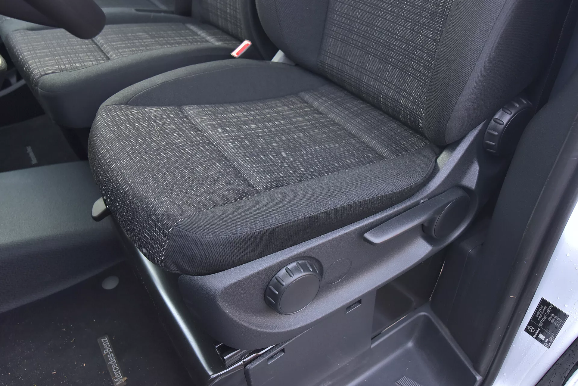 Interiér Mercedes-Benz Vito 2014 Tourer se zaměřením na spolujezdcovo sedadlo s odolným tmavým potahem, knoflíkem pro manuální nastavení a bezpečnostními prvky jako je jasně viditelný přijímač bezpečnostního pásu.