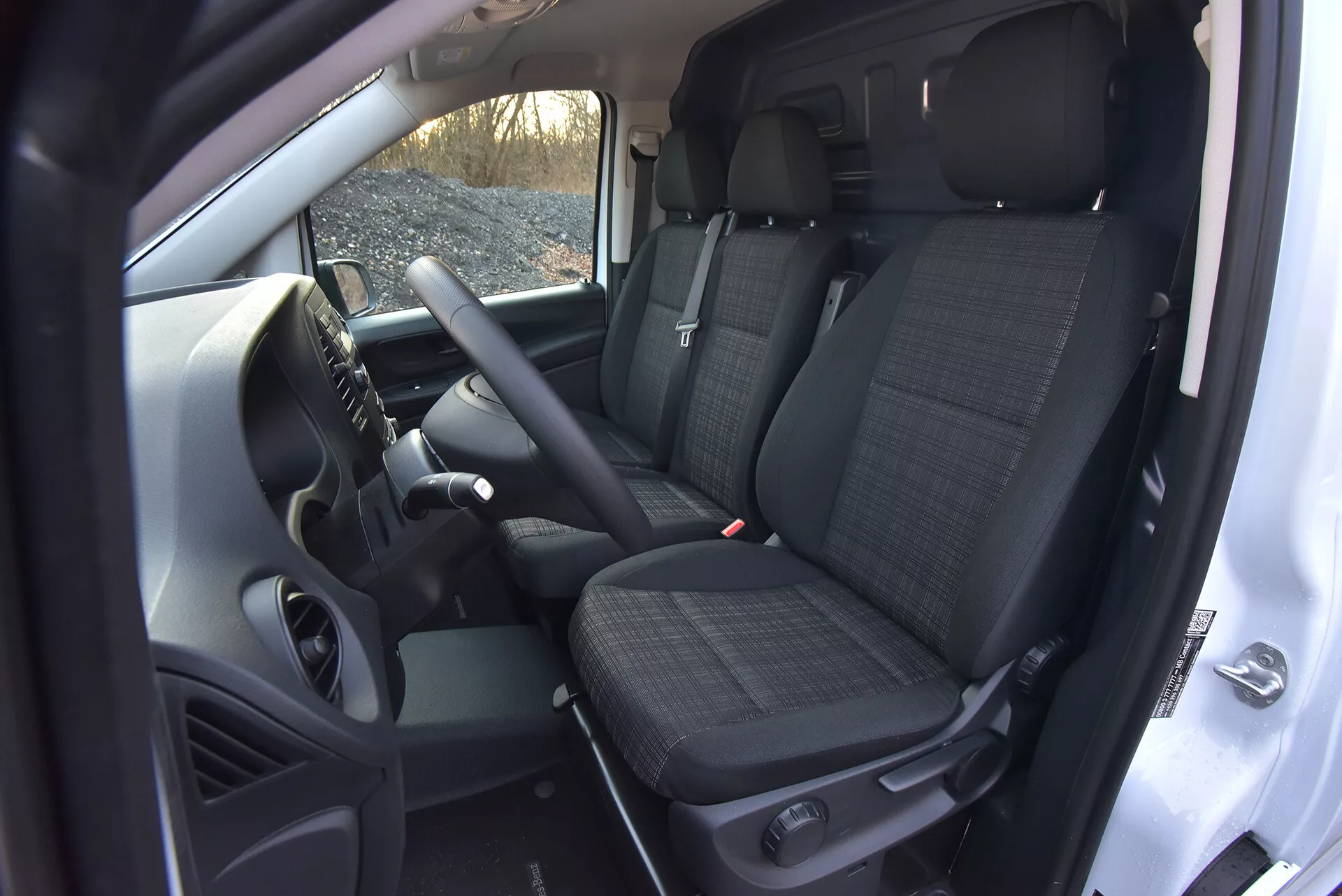 Interiérový pohled na Mercedes-Benz Vito 2014 (Vito-Tourer) ukazující oblast řidiče a spolujezdce s technologickými prvky jako ovládání na volantu, centrální konzoli možná obsahující informačně-zábavní systém, přední sedadla s potahem z vzorované látky s opěrkami hlavy a pohledem na zadní sedadla, vše z vysokého úhlu zdůrazňující prostornost kabiny a prvky manuální převodovky.