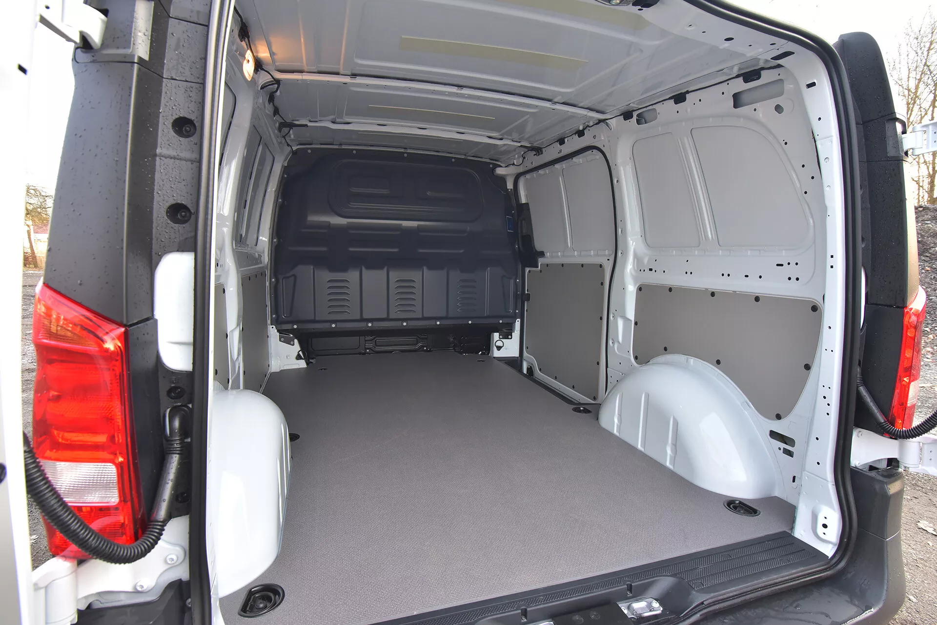 Zadní nákladový prostor obchodního dodávky Mercedes-Benz Vito Tourer 2014 s otevřenými dveřmi, ukazující plochou odolnou podlahu a holý kovový interiér pro snadnou úpravu, zobrazený z mírně zkoseného zadního vnějšího úhlu