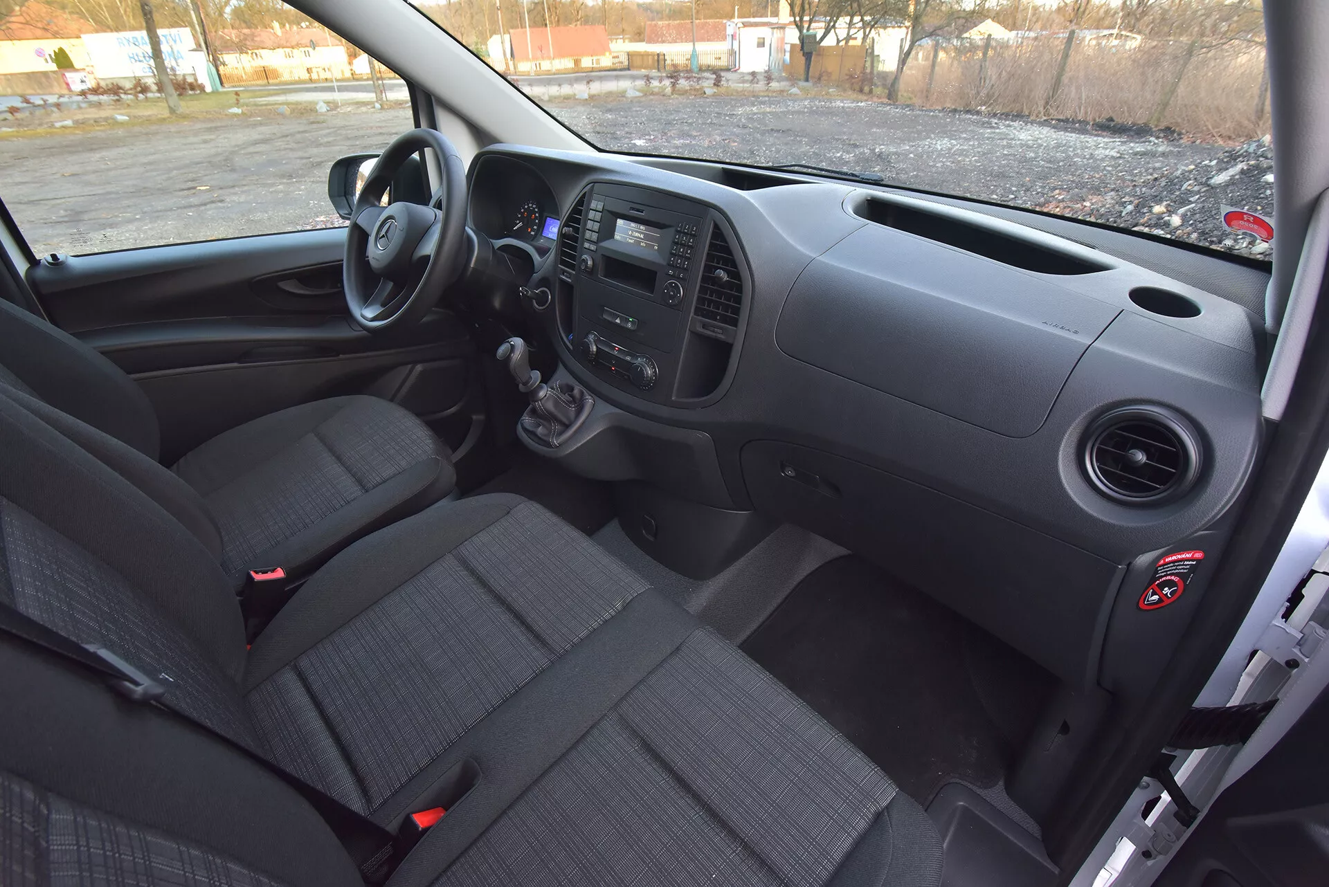 Interiér Mercedes-Benz Vito Tourer z roku 2014 z pohledu řidiče s předním palubním panelem, manuální převodovkou, ovládacími panely a sedadly s potahem