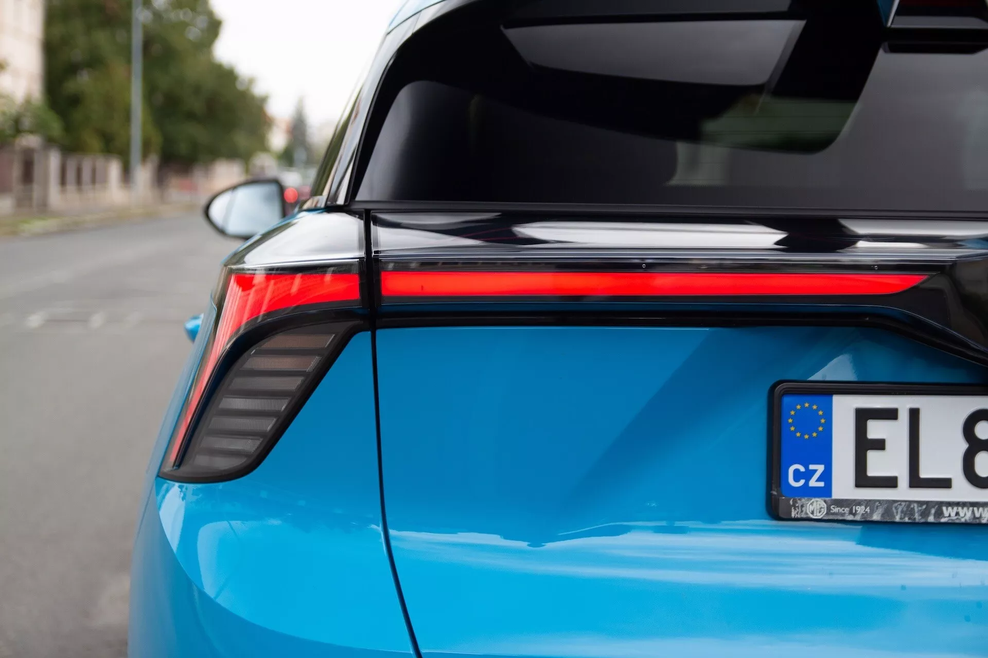 Detailní pohled na zadní část světle modrého vozu MG MG4 rok 2022, zobrazující LED zadní světlo, elegantní designové křivky, lesklý povrch a integrované zadní křídlo, což naznačuje moderní prvky automobilového designu a efektivity.