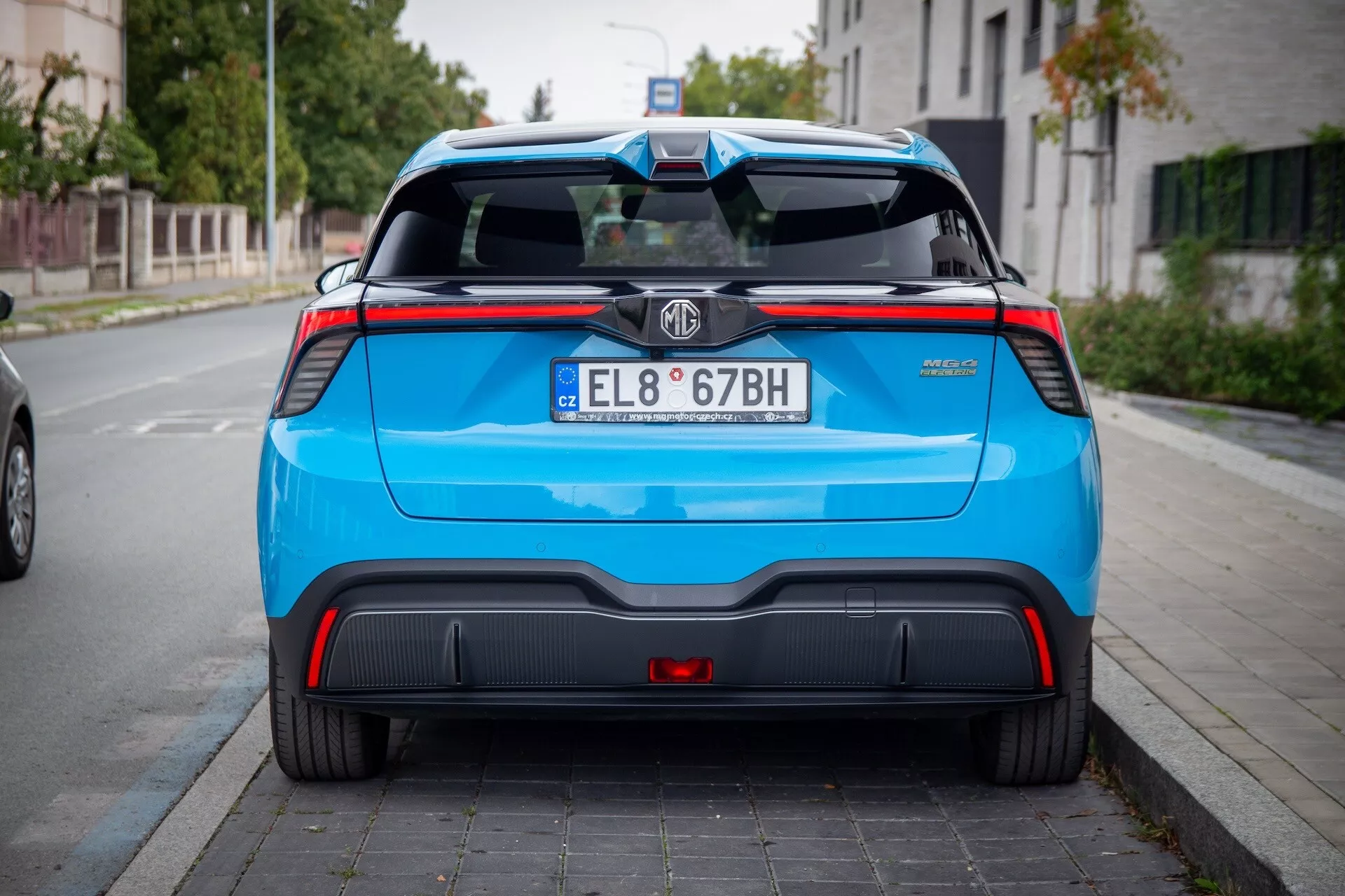 Zadní pohled na MG MG4 2022 v živě modré barvě, předvádějící sportovní prvky včetně LED zadních světel, zadního spoileru, nárazníku s černými a červenými akcenty a emblému výrobce na zadních dveřích zaparkovaný na městské ulici.