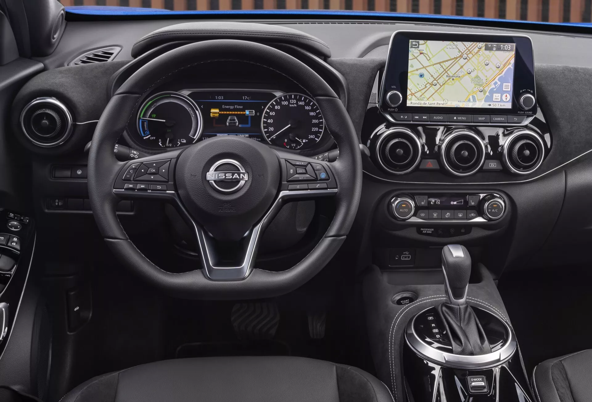 Vnitřní pohled na Nissan Juke (F16) z roku 2019, zvýrazňující palubní desku, vícefunkční tříramenný volant s logem NISSAN, kombinovaný digitálně-analogový přístrojový panel, dotykový multimediální systém s navigací, klimatizaci s dvojzónovou regulací a oblast automatického voliče převodů.