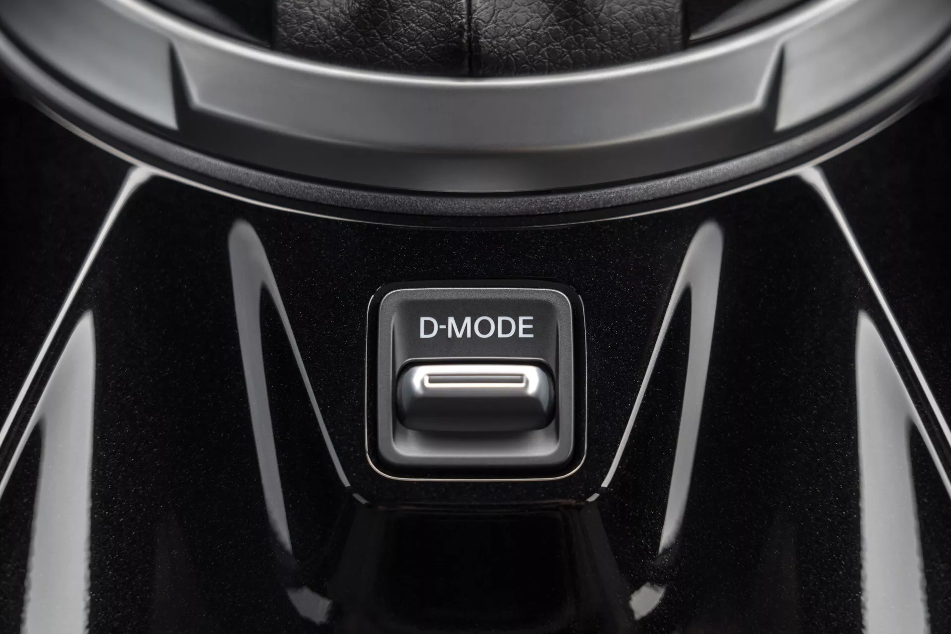 Detailní pohled na tlačítko D-MODE ve středové konzoli Nissan Juke 2019 (F16), s vysokým leskem černého povrchu a chromovanými akcenty pod světlem shora