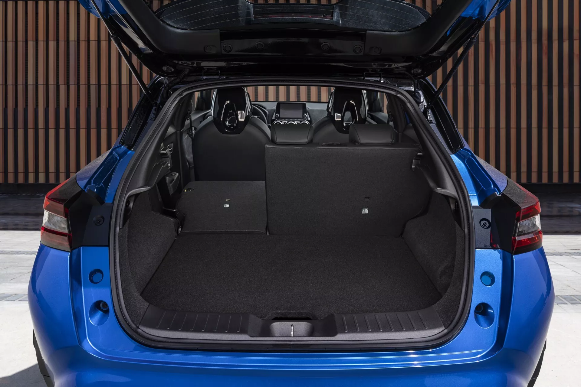 Nissan Juke (F16) z roku 2019 s prostorným a prázdným kufru se zvednutým víkem, detailní pohled do nákladového prostoru s kobercovým čalouněním, obklopeným charakteristickými červenými zadními světly a moderními designovými prvky exterieru, z přímého zadního pohledu.