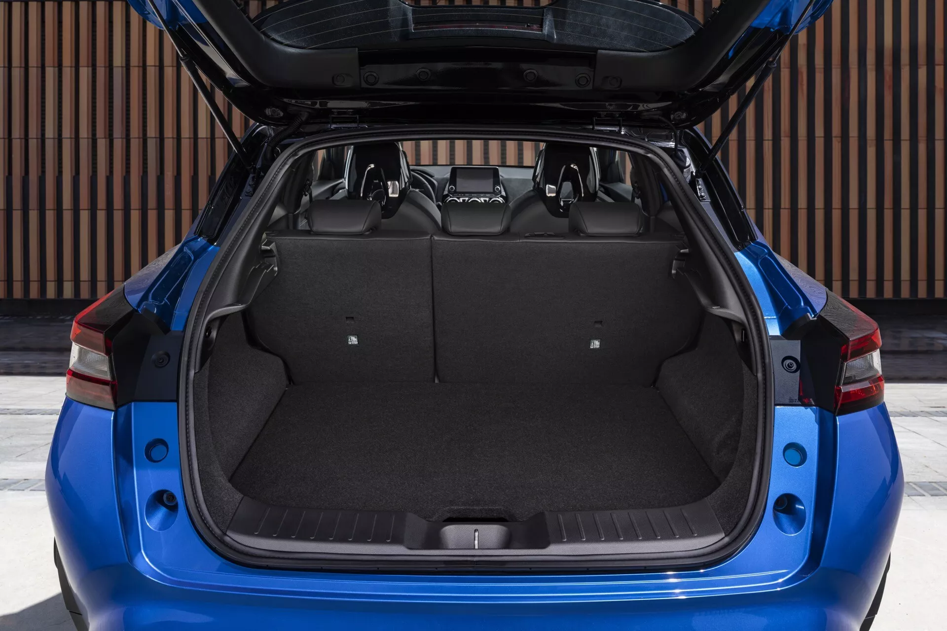 Zadní pohled na modrý Nissan Juke z roku 2019 F16 s otevřeným kufrerm a ukazujícím nákladový prostor a designové prvky ve dne