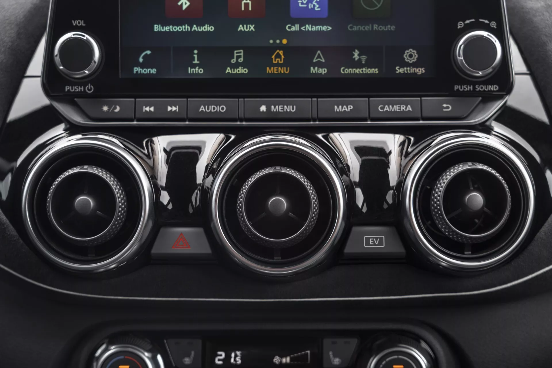 Detailní pohled na středovou konzoli Nissan Juke (F16) z roku 2019 s ovládáním klimatizace, informačním systémem s dotykovou obrazovkou včetně režimu EV, kovovými ventilačními mřížkami a panelem klimatizace