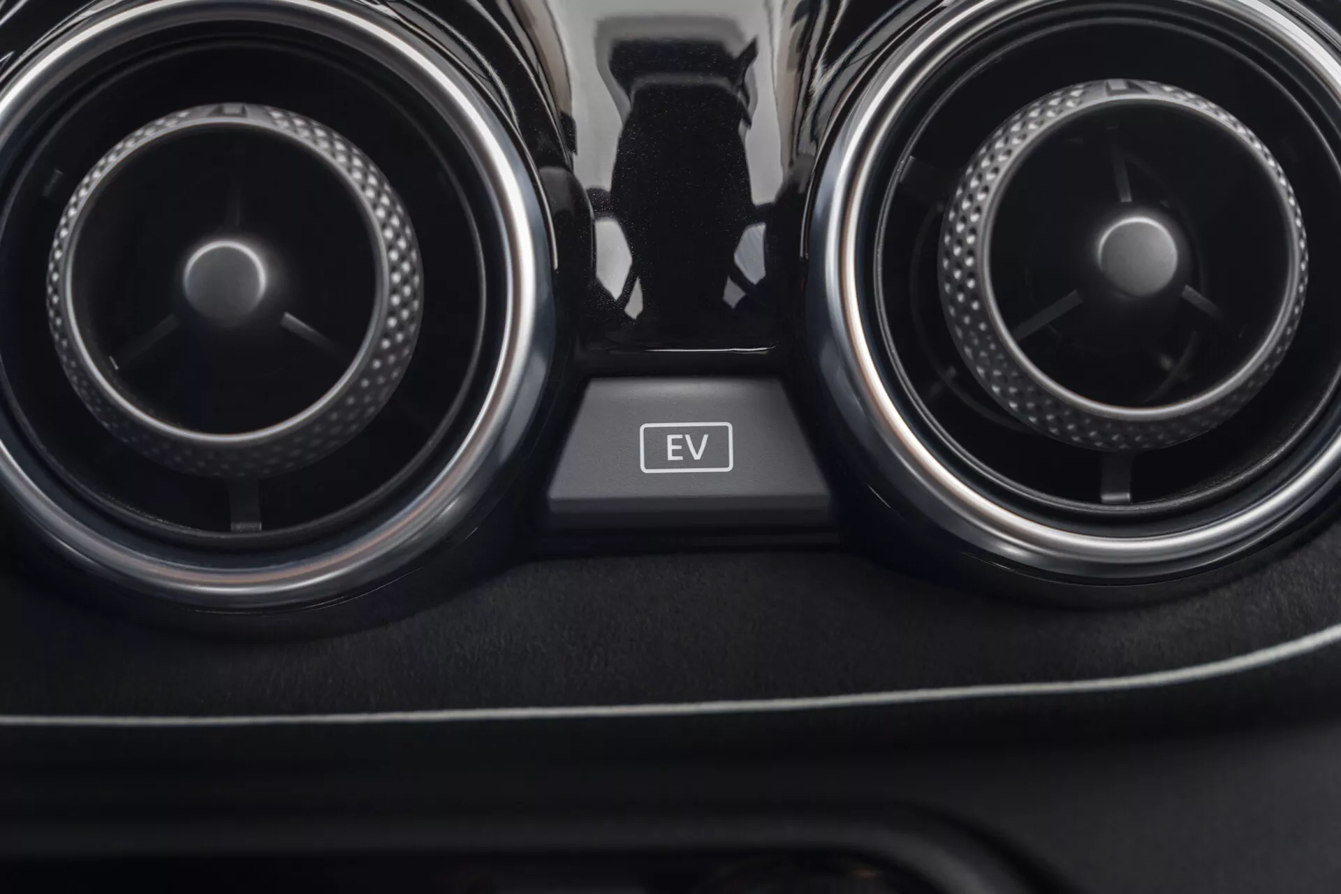 Detailní pohled na interiér Nissan Juke 2019 (F16) zaměřený na ventilační otvory klimatizace a tlačítko režimu EV mezi nimi, předvádějící kontrolu klimatu v autě a technologii elektrických vozidel.