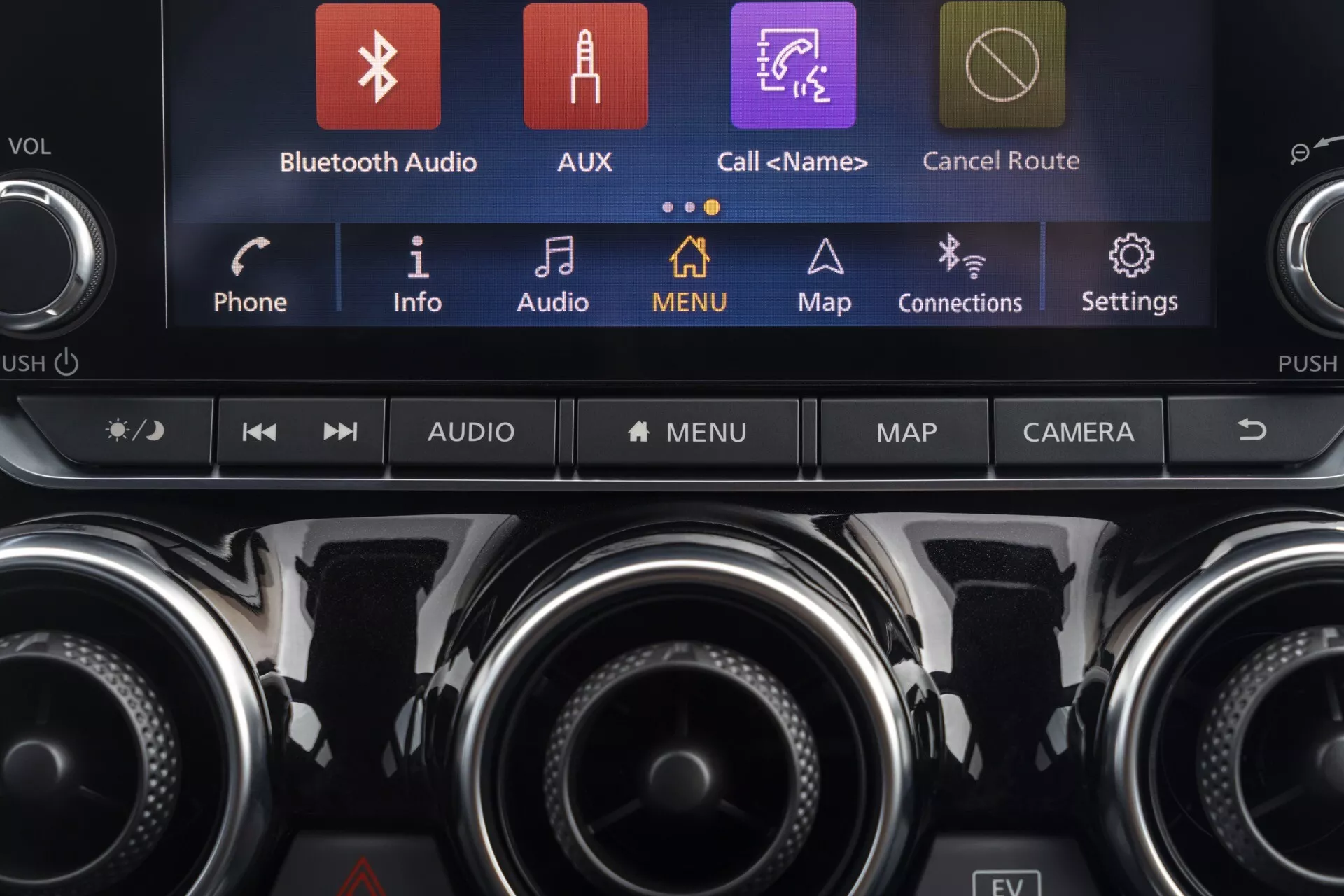 Detailní pohled na centrální konzolu Nissan Juke (F16) 2019 s dotykovým informačním systémem zobrazujícím barevné ikony jako Bluetooth Audio, AUX a Mapy, spolu s ovladači klimatizace a dalšími funkčními tlačítky, zdůrazňující moderní technologie vozidla a prémiový interiér