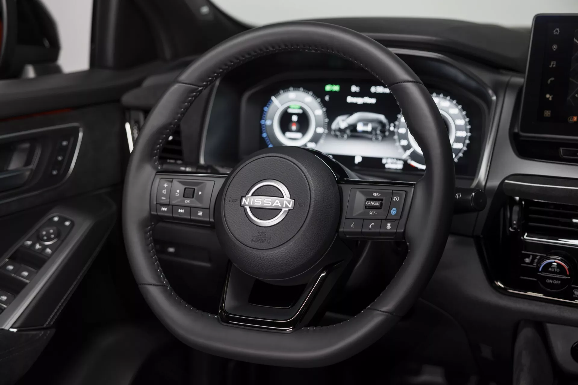 Interiér Nissan Qashqai 2024 (J12 facelift) zaměřený na volant a digitální přístrojovou desku, představující tříramenný kožený volant s multifunkčními tlačítky a rozsáhlý LCD displej zobrazující různé diagnostiky vozidla a informace pro řidiče, pořízený z perspektivy zadního sedadla uprostřed.