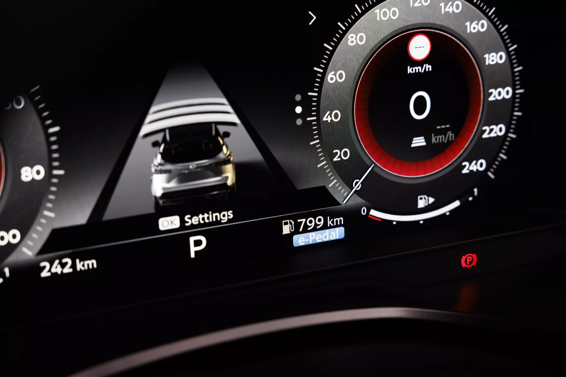 Tento obrázek ukazuje přístrojovou desku a digitální displej vozu Nissan Qashqai 2024 (J12-facelift) z pohledu řidiče, se zaměřením na pravou stranu. Digitální displej zobrazuje grafiku auta shora naznačující asistenční parkovací systém nebo senzorově-založenou bezpečnostní funkci, s interaktivními nastaveními kolem. Analogový tachometr s ručičkou na '0' a digitální údaj rychlosti '0 km/h' je integrován do displeje, kalibrován do 220 km/h. Pod údajem o rychlosti jsou uvedeny dojezd '799 km' a funkce 'e-Pedal' související s technologií elektrických vozidel. Horizontální čára vlevo naznačuje úroveň nabití baterie. Viditelné jsou také celkové kilometry vozu ('242 km') a režim 'P' pro Park. Moderní estetika zdůrazňuje pokročilé asistenční systémy řidiče, s vysokým kontrastem barev, především černé a červené. Relevantní pro automotive technologie, přístrojové panely vozidel, elektrická vozidla a asistenční systémy řidiče.