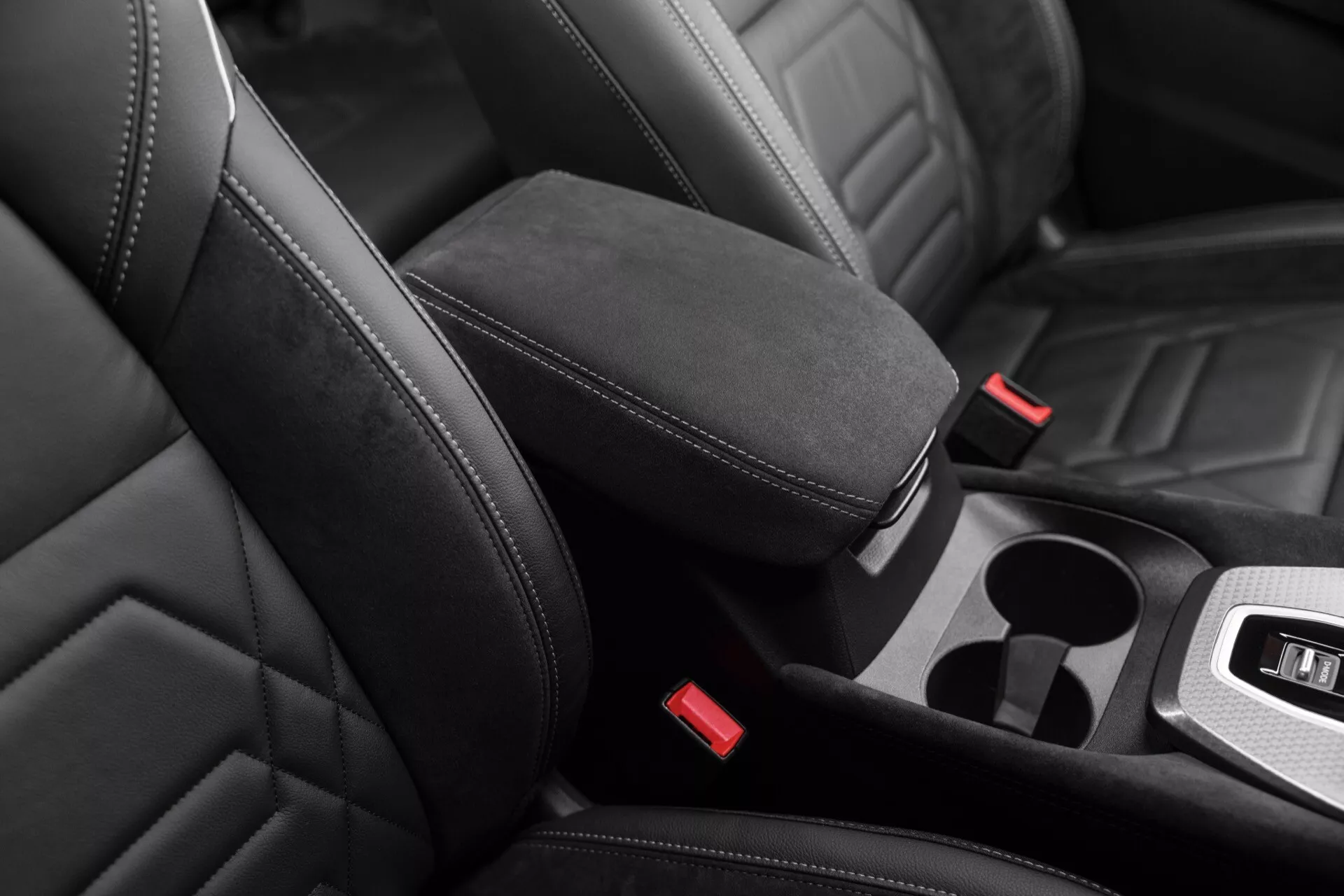 Detailní pohled na interiér vozu Nissan Qashqai 2024 (J12-Facelift), který zvýrazňuje moderní kožené čalounění a výrazné prošívání předního sedadla spolujezdce a částečně řidičského sedadla z šikmého nadhledu. Červené spony bezpečnostních pásů kontrastují s tmavšími sedadly, včetně integrované středové opěrky a potenciálního úložného prostoru nebo držáků na nápoje. Rovnoměrné osvětlení zdůrazňuje kontury sedadel a kvalitu materiálu, což naznačuje prémiový design.