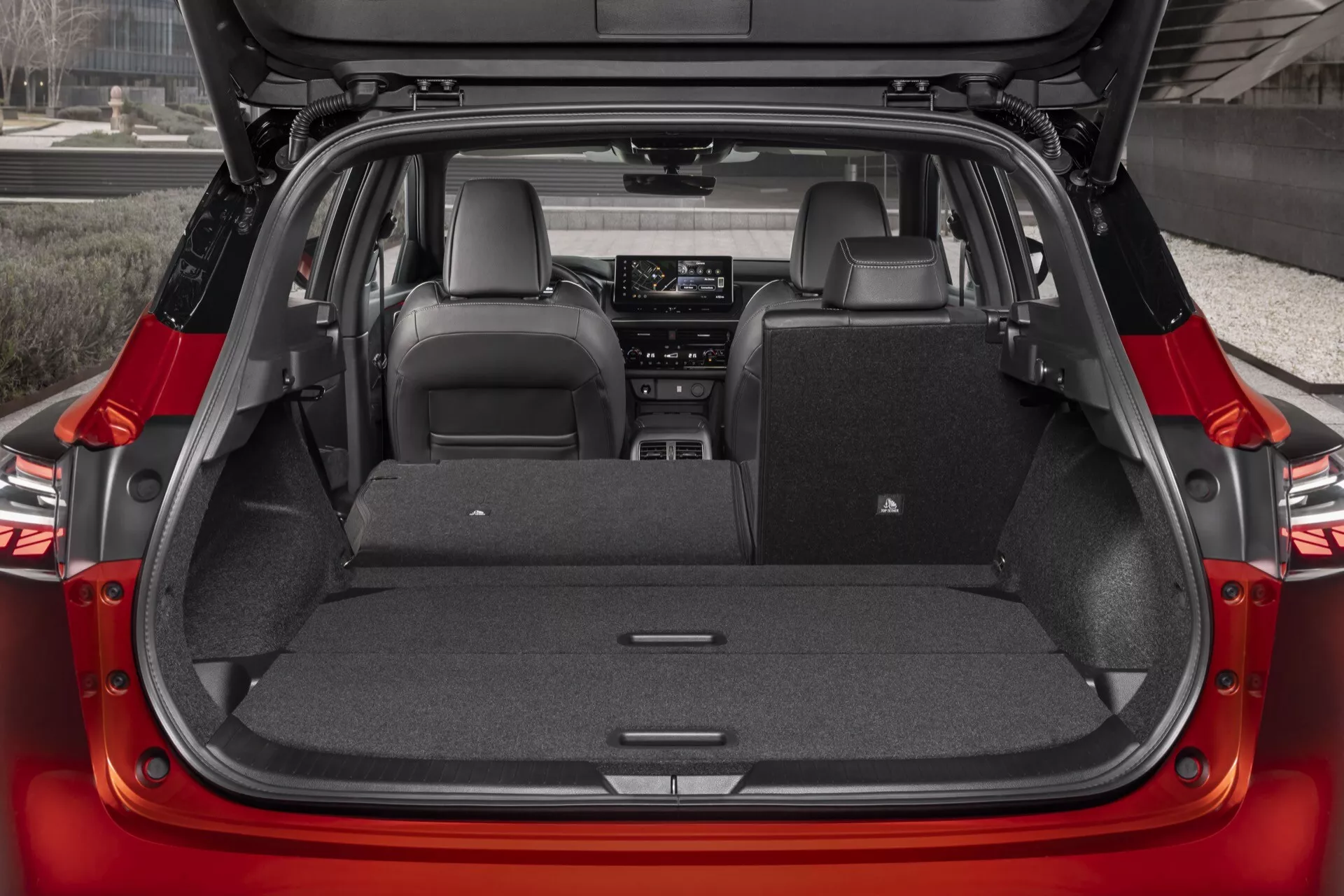Interiér zavazadlového prostoru Nissan Qashqai 2024 (J12-facelift) z pohledu zezadu s otevřeným zadním víkem, ukazující rovnou nákladovou podlahu a sklápěcí zadní sedadla v poměru 60/40, s tmavým čalouněním a zaměřením na prostorný, moderní design.