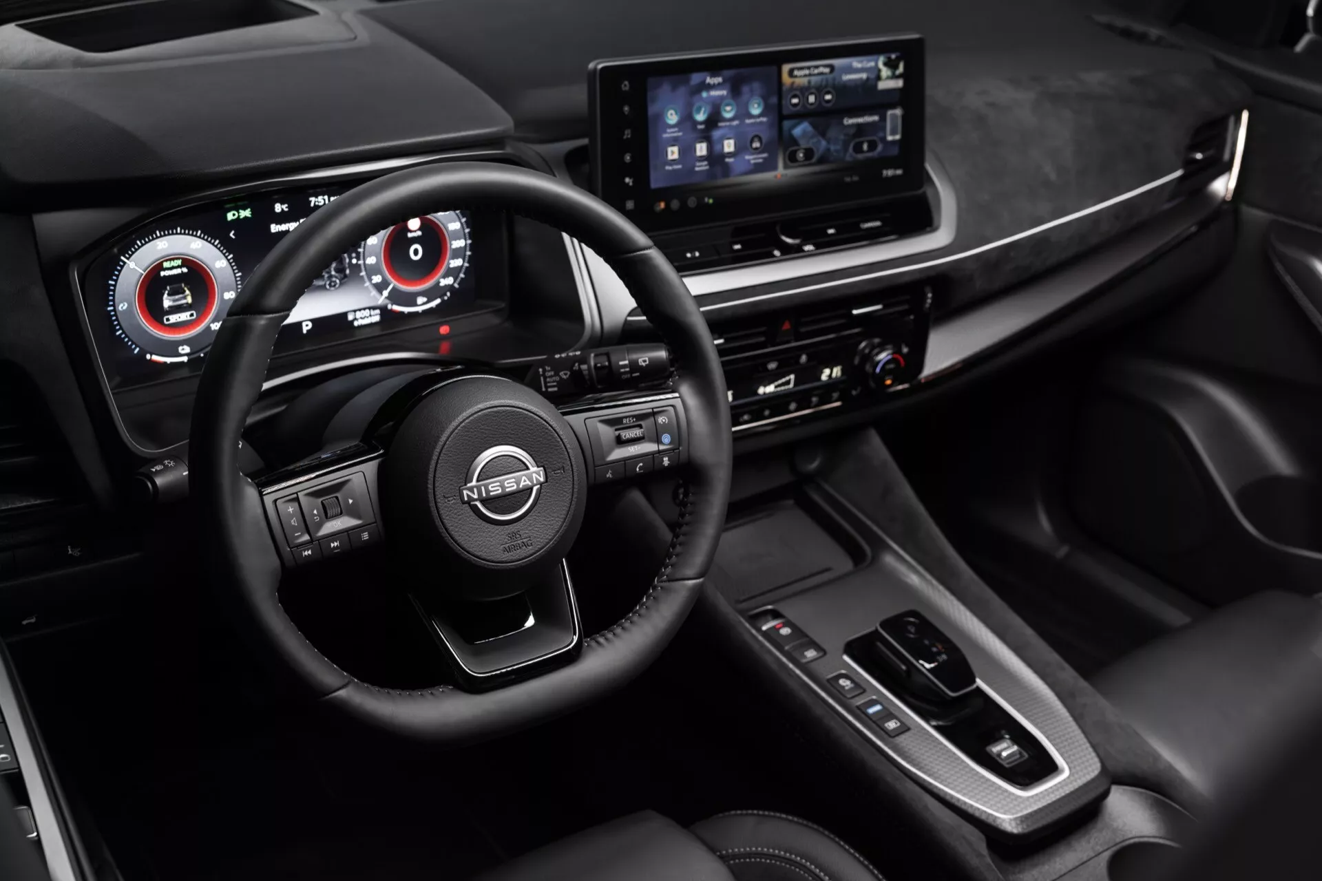 Pohled na interiér vozu Nissan Qashqai 2024 (J12-Facelift) na palubní desku a oblast volantu ze mírně zvýšeného, zprava posunutého úhlu. Vlastnosti zahrnují tříramenný multifunkční volant, dvouobrazovkový infotainment systém, analogové přístrojové skupiny s digitálními displeji, koženou řadicí páku, horizontální řadu tlačítek na konzoli a směsice kožených čalounění, kovových akcentů a falešného dřeva v tmavé barevné paletě zdůrazňující ergonomický design a pokročilé technologie.
