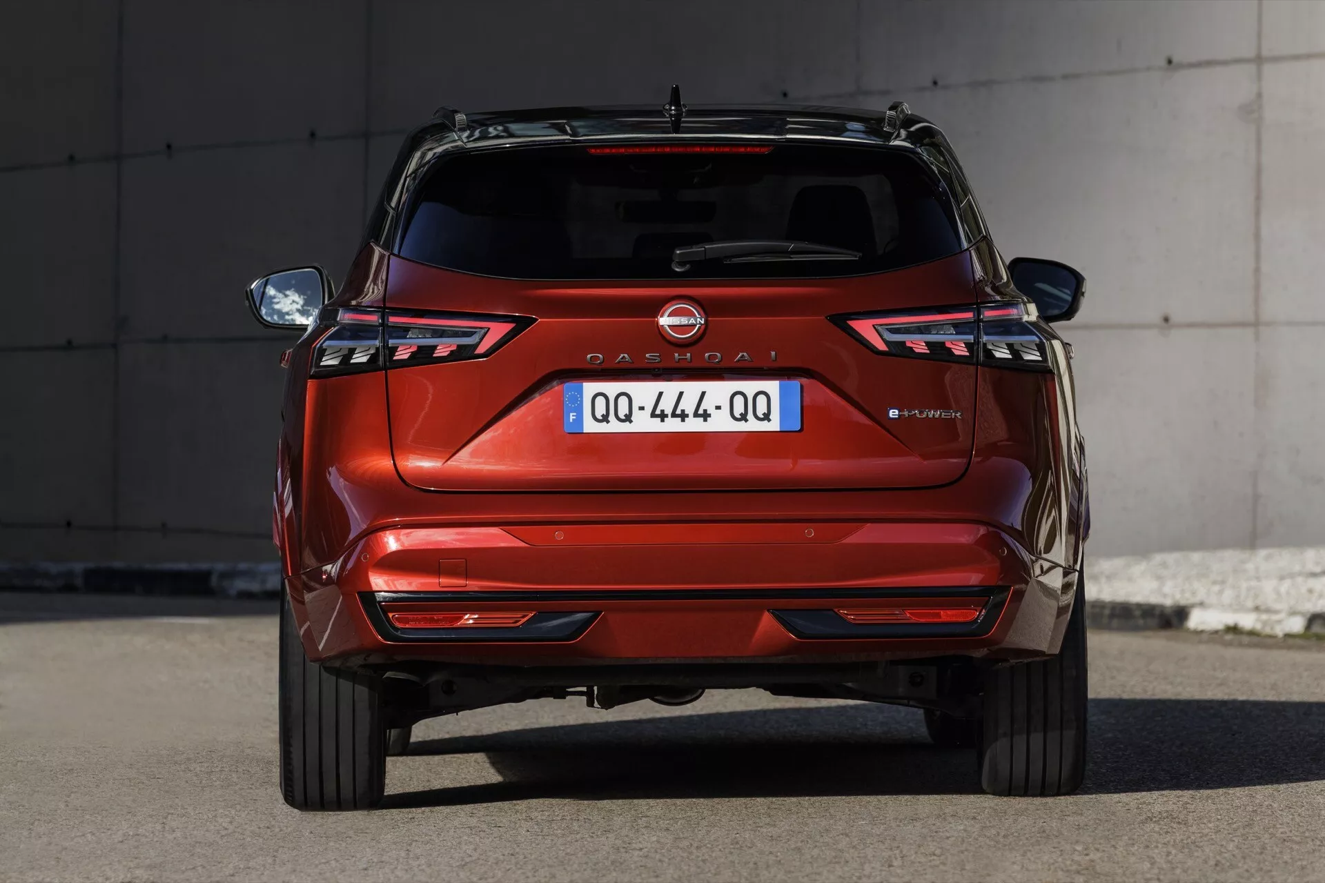 Zadní pohled na zaparkovaný Nissan Qashqai 2024 (J12-Facelift) prezentující moderní designové prvky jako stylizované LED zadní světlomety s charakteristickým tvarem, dvojité výfukové potrubí a centrálně umístěnou evropskou registrační značku, vše osvětleno denním světlem.