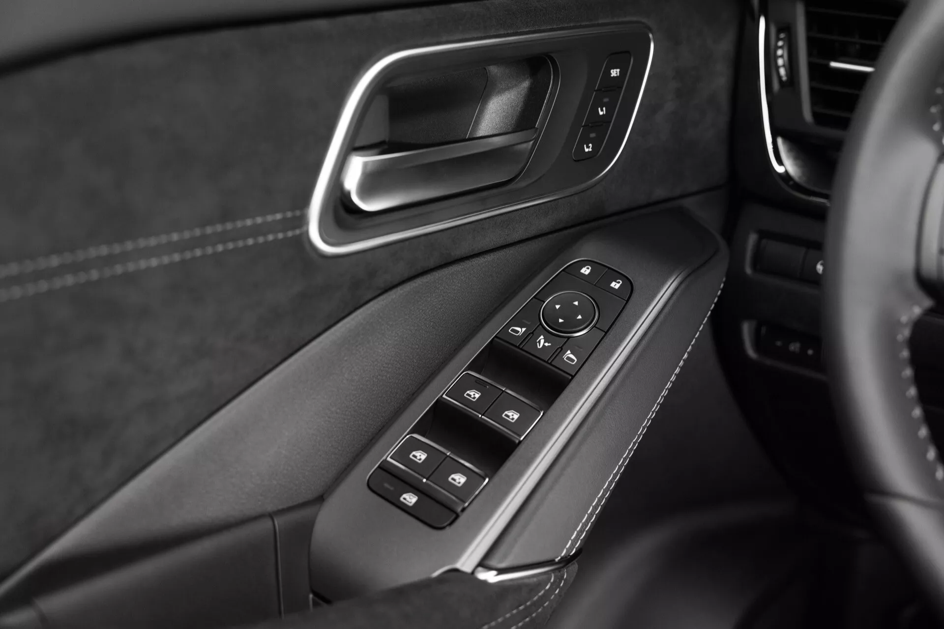 Detailní záběr interiérového panelu dveří modelu Nissan Qashqai 2024 (J12-facelift), zvýrazňující ovládací panel pro elektrická okna a boční zrcátka umístěný na opěrce ruky. Fotografie se zaměřuje na ovládací prvky včetně tlačítek elektrických oken s funkcí auto-dolů, zámku oken a nastavení bočních zrcátek pomocí směrového joysticku. Panel je doplněn kartáčovaným kovem a materiály podobnými kůži s viditelným šitím, což podtrhuje řemeslné zpracování a prémiovou kvalitu. Monochromatický obrázek zdůrazňuje funkčnost a detaily designu.