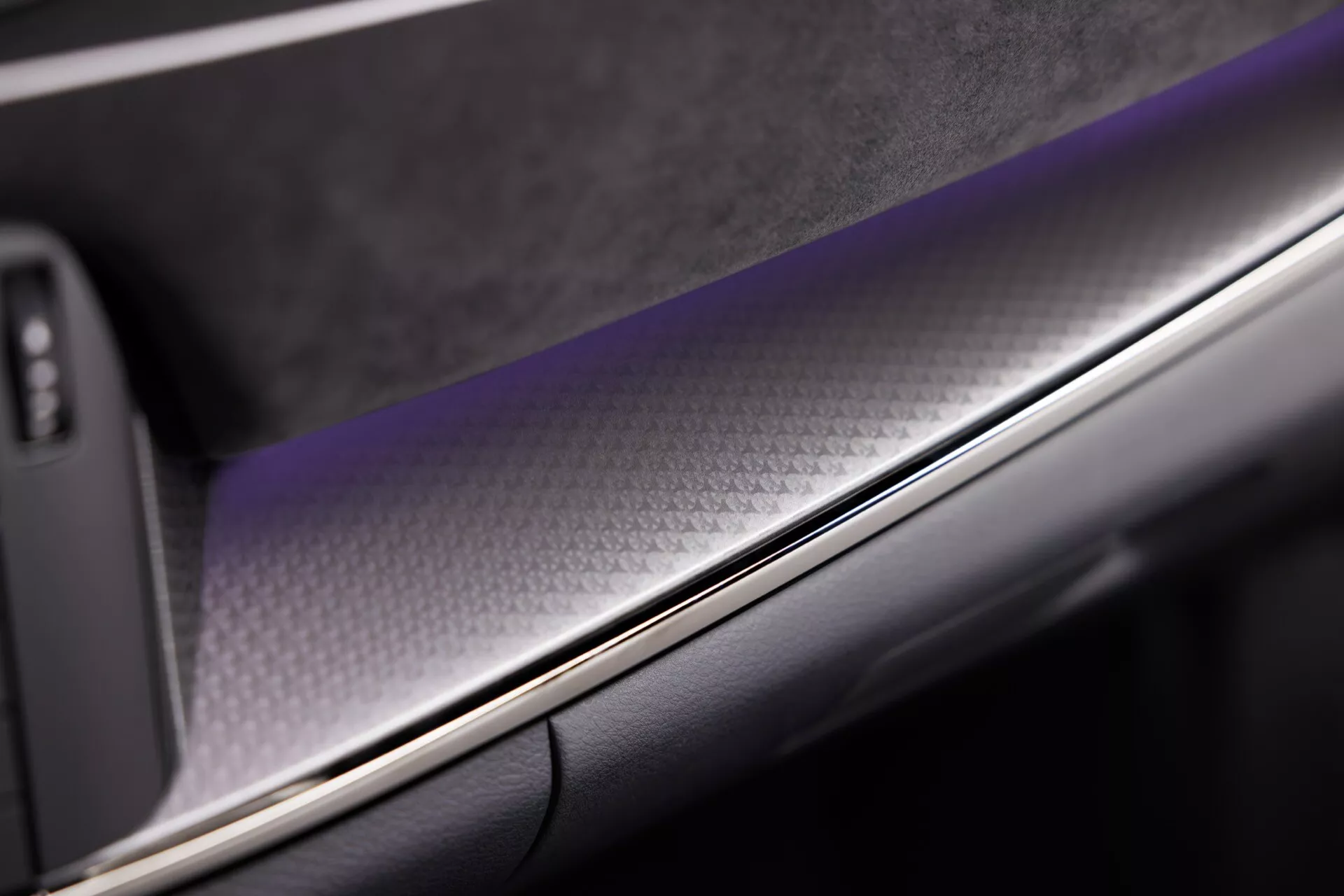 Detailní záběr na interiér vozu Nissan Qashqai 2024 (J12-Facelift), zdůrazňující část přístrojové desky nebo dveřního panelu s vzorovaným materiálem připomínajícím uhlíkové vlákno, chromovaným pruhem a koženým nebo koženkovým povrchem, což podtrhuje luxus a zpracování.