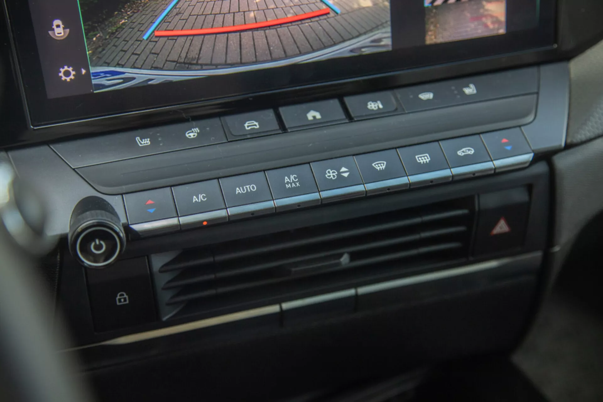Centrální konzole a panel klimatizace Opel Astra 2022, zdůraznění ovladače teploty, rychlosti ventilátoru, rozdělení vzduchu a tlačítek automatické klimatizace s digitálním displejem zobrazujícím zadní kameru