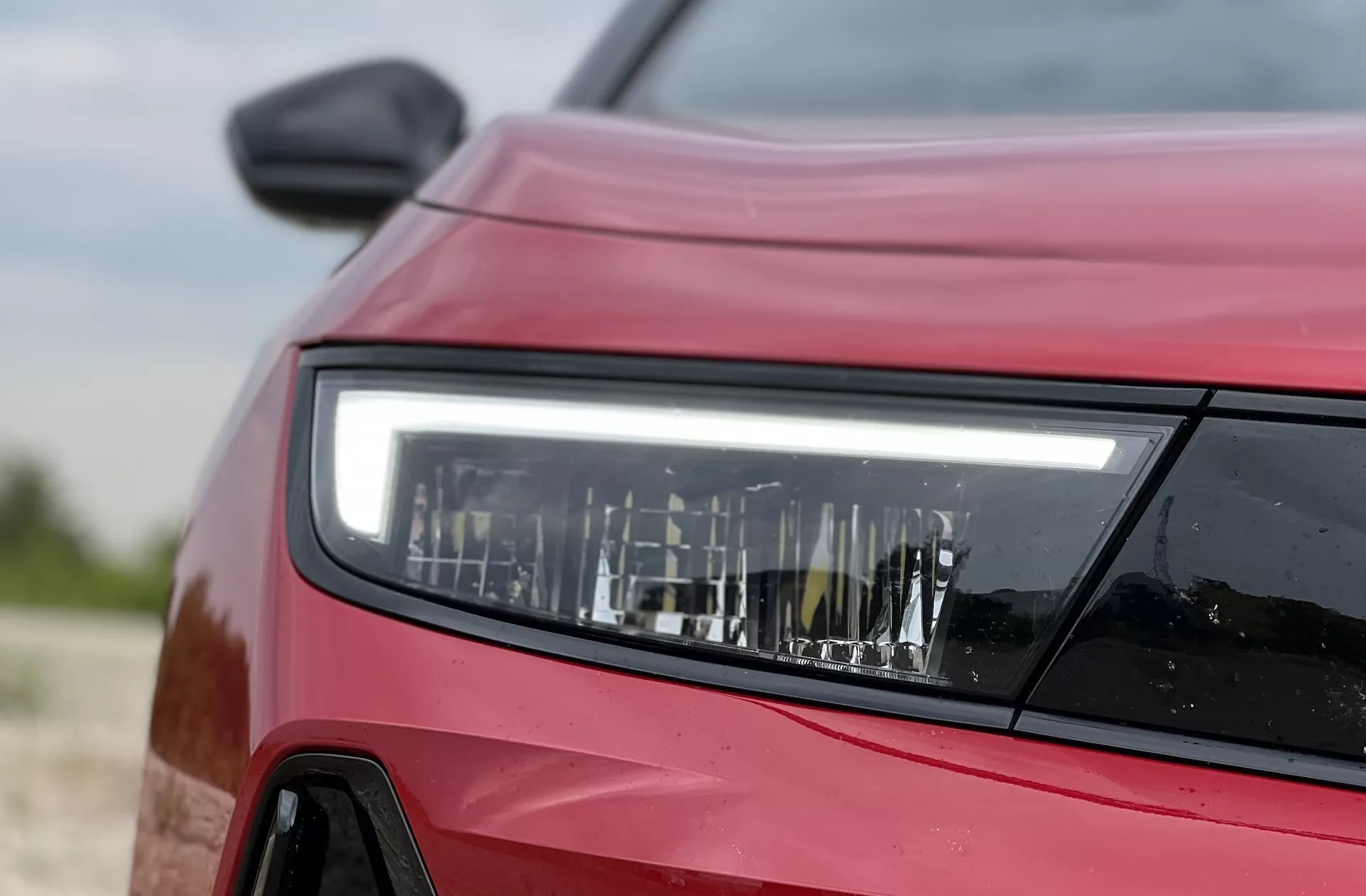 Detailní pohled z přední strany na červený Opel Astra 2022 s důrazem na podrobný design LED světlometu, který ukazuje moderní technologii osvětlení a obrysy vozidla