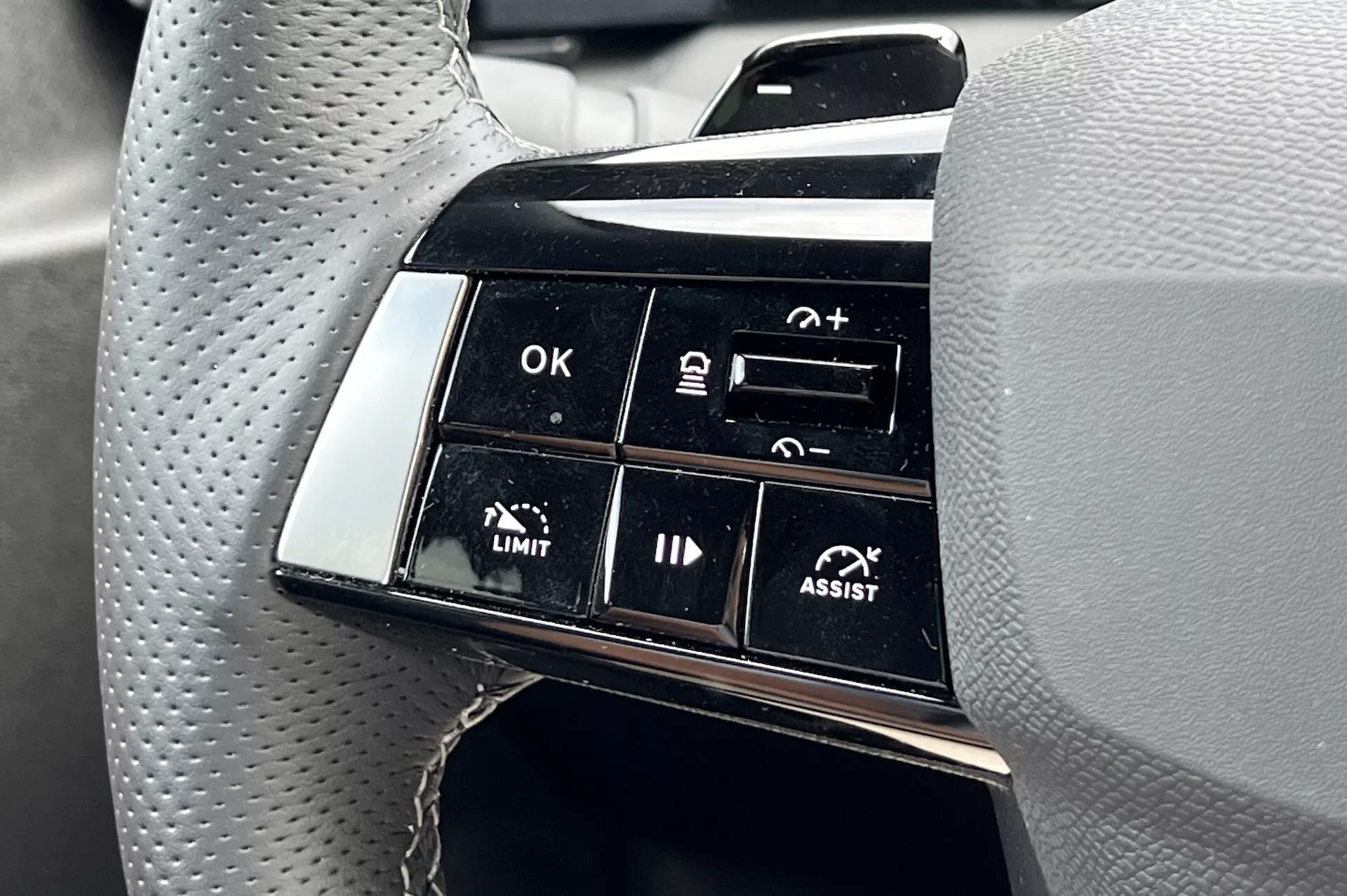 Detailní pohled na ovladače na volantu Opel Astra 2022 s důrazem na pokročilé funkce asistenčních systémů řízení včetně adaptivního tempomatu a asistence udržování jízdního pruhu s popisky funkcí jako OK, +, -, LIMIT a ASSIST z pohledu řidiče