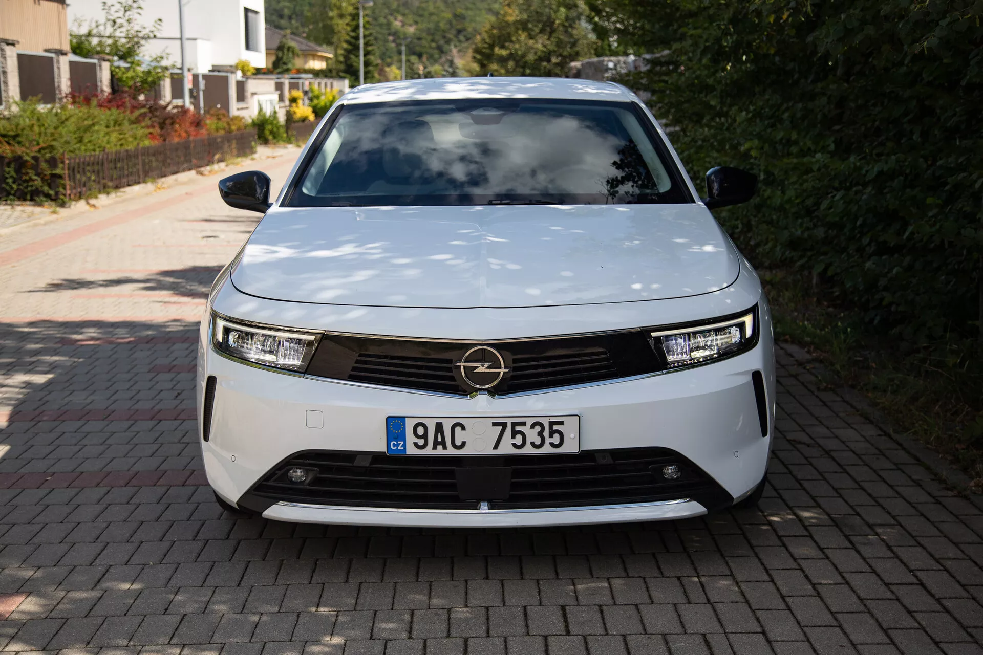 Čelní pohled na Opel Astra 2022 představující moderní design elektrického vozidla s LED světlomety, dekorativní mřížkou a aerodynamickým tvarem, zaparkované na příjezdové cestě rodinného domu