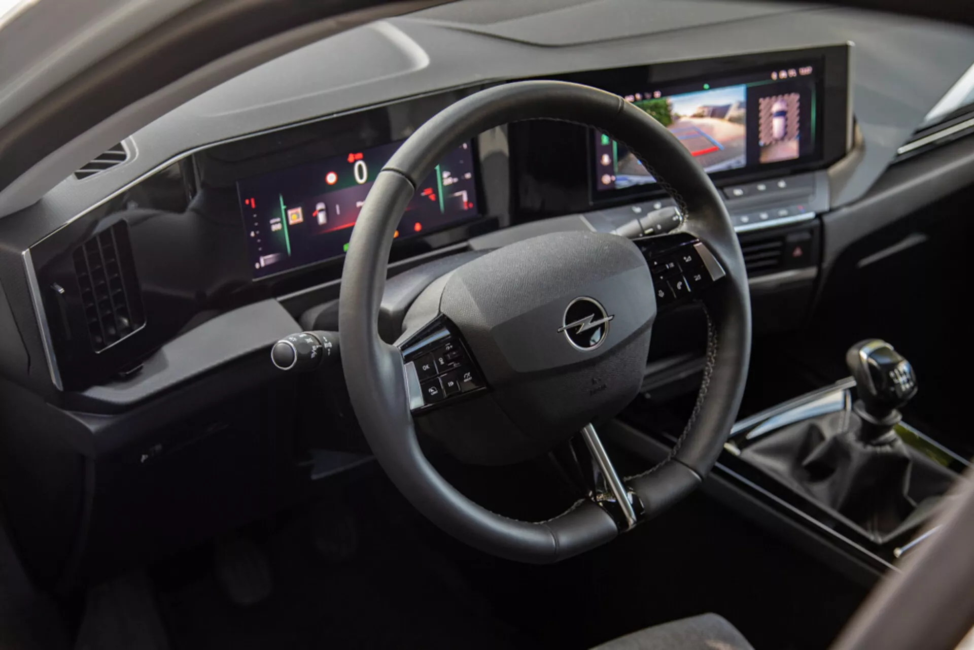 Interiér Opel Astra 2022 zobrazující prostor řidiče s volantem se třemi rameny, digitálním palubním panelem a centrální konzolí včetně dotykového infotainment systému, manuální převodovky a moderních ovládání klimatizace
