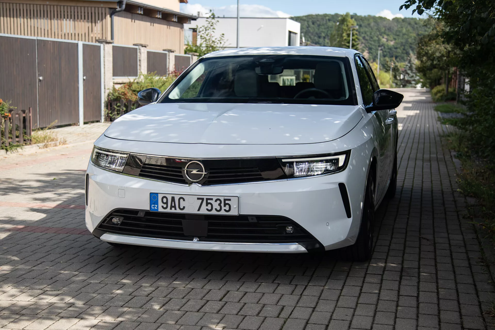 Pohled zepředu a ze strany na Opel Astra 2022 s LED světlomety, minimalistickým designem mřížky, částečně viditelnými slitinovými koly a hladkými karosářskými panely na evropské obytné ulici