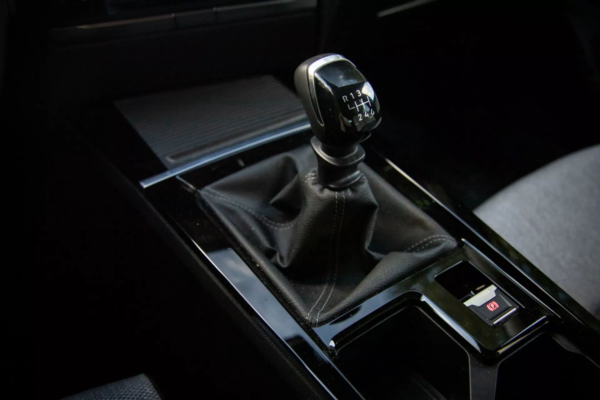 Detailní pohled na manuální převodovku automobilu Opel Astra 2022 v pravém horním rohu snímku s koženým krytem, lesklou černou konzolou a okolními prvkami interiéru
