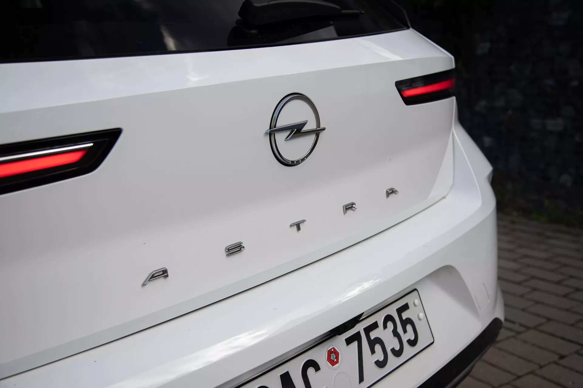 Detailní pohled na zadní část bílého Opelu Astra rok 2022, zdůrazňující LED zadní světla, logo Opel a název modelu 'ASTRA' na víku zavazadlového prostoru