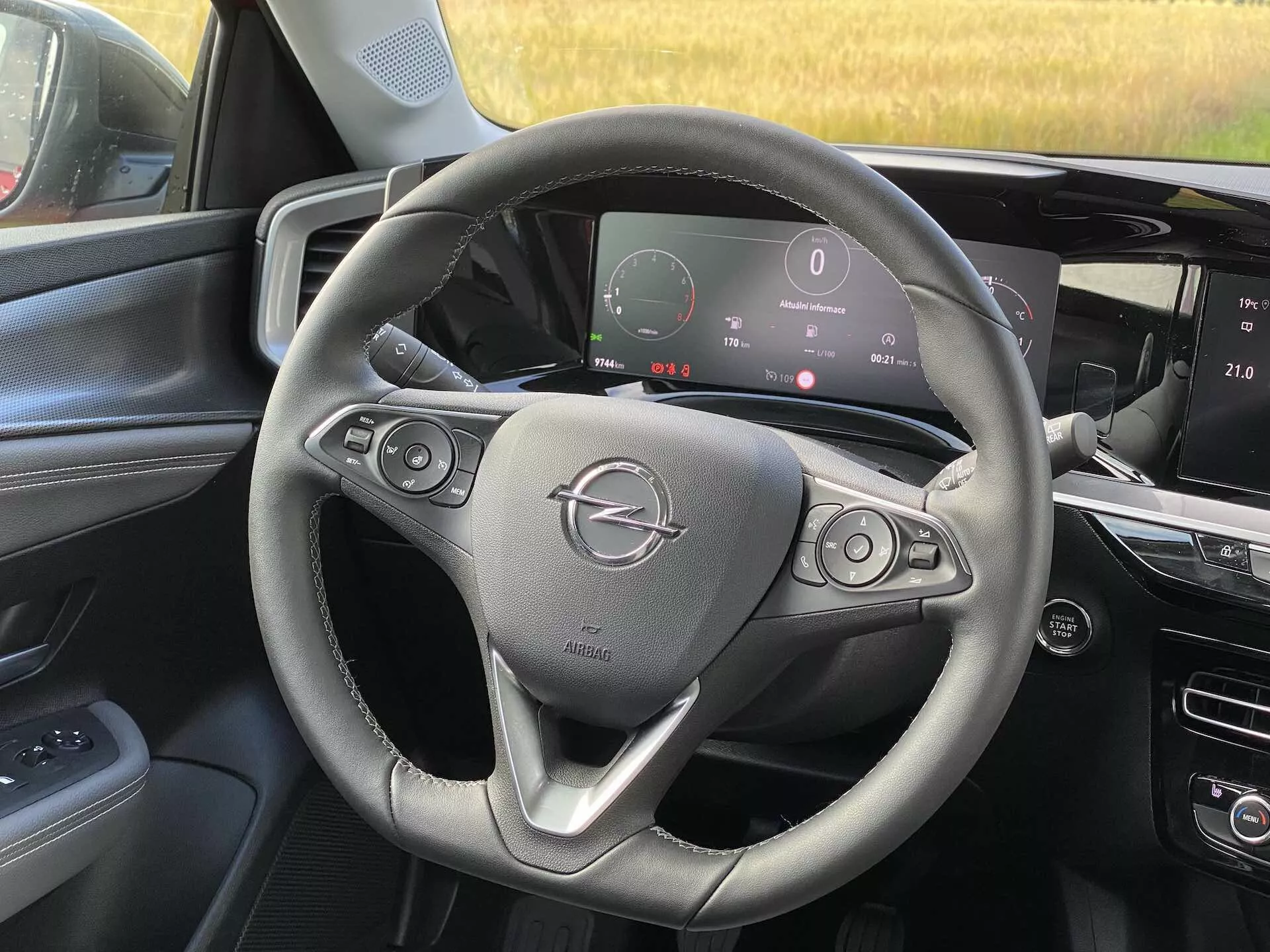 Interiér pohled na Opel Mokka 2021 z perspektivy předního spolujezdce, ukazující volant s tlačítky pro ovládání zvuku a tempomatu, digitální přístrojovou desku zobrazující tachometr a další metriky, a středovou konzoli s dotykovým infotainment systémem.